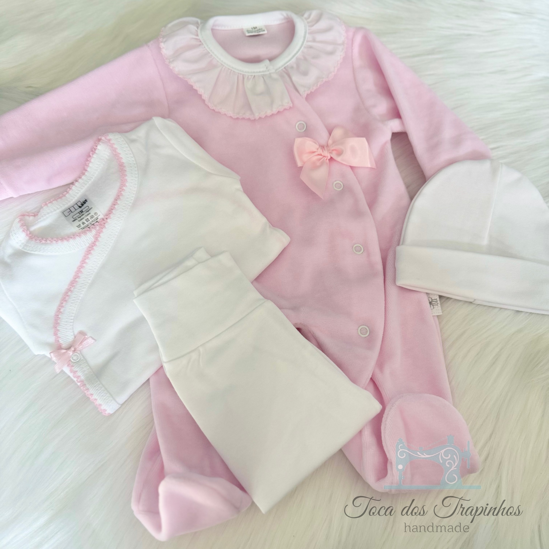 Conjunto de roupa de bebé rosa e branca sobre superfície branca felpuda
