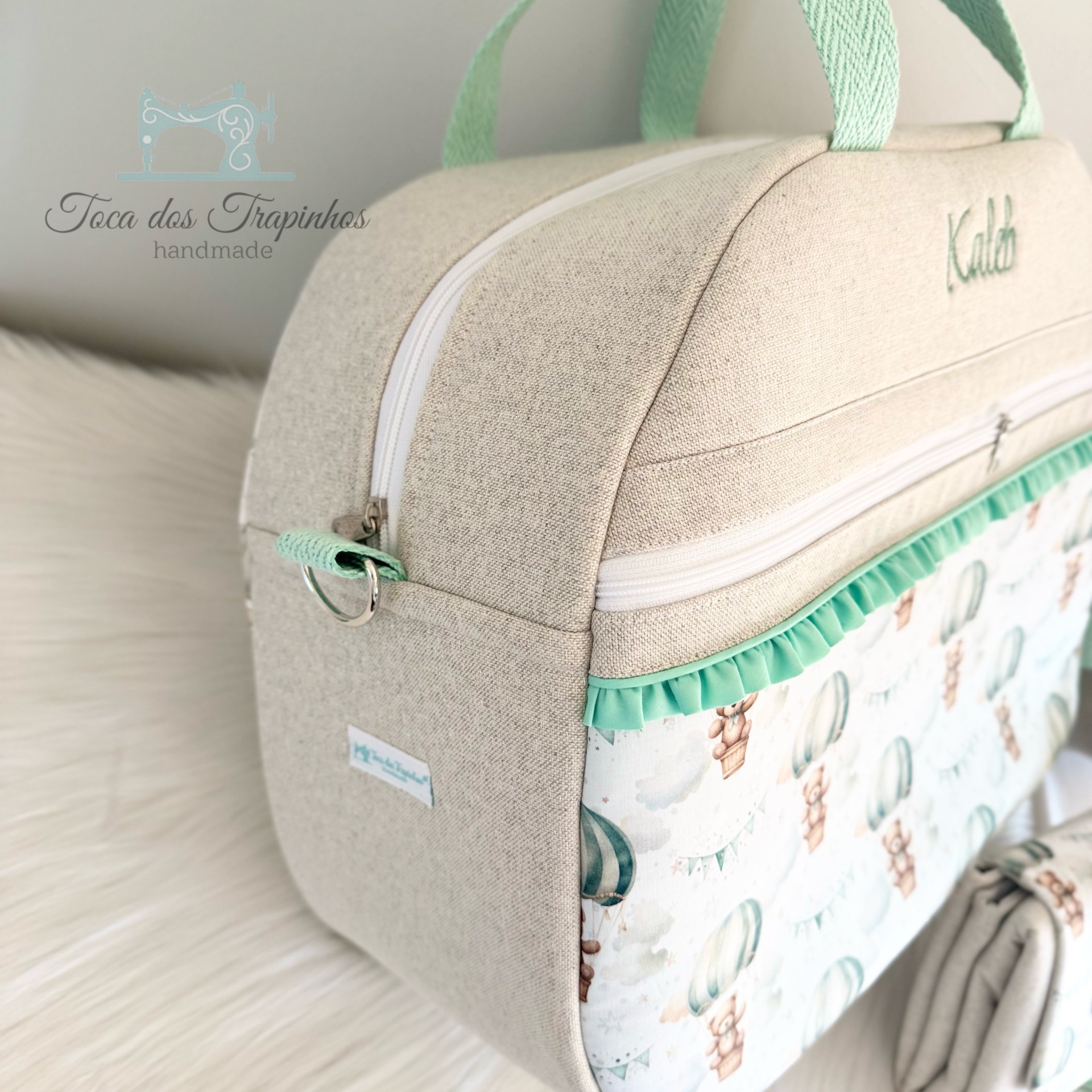 Mala bege com padrão de balões e ursos, fechos brancos e alças verdes.