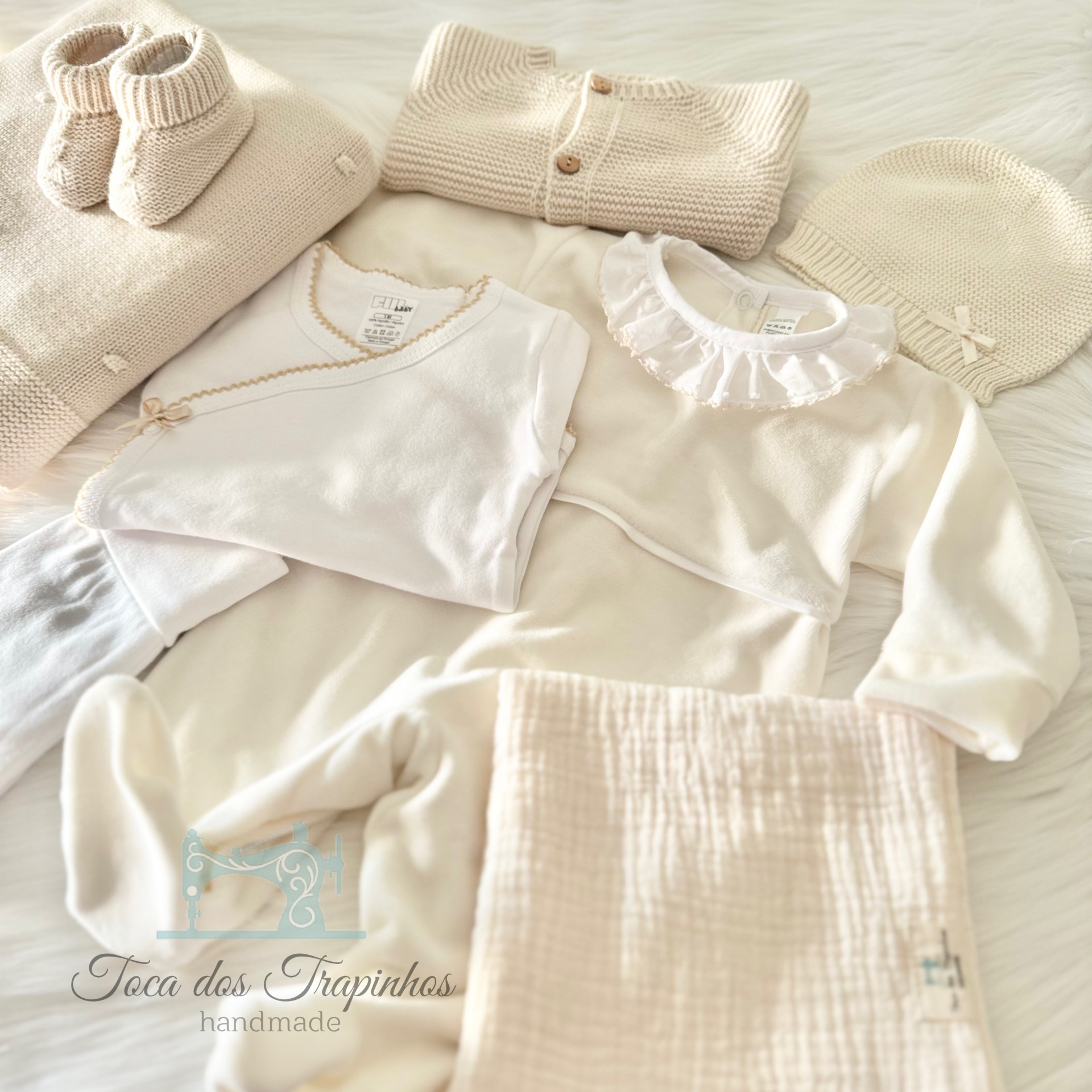 Conjunto de roupa para bebé creme e branco com várias peças e manta sobre fundo claro peludo