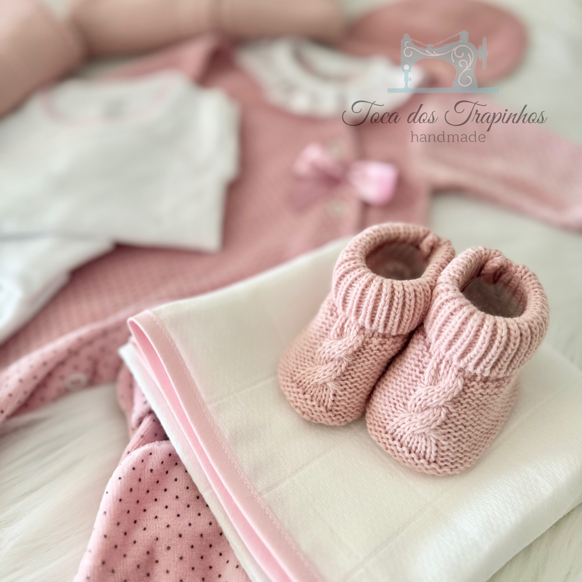 Conjunto de roupa de bebé com body branco, casaco e calças rosas, sapatinhos de malha rosa
