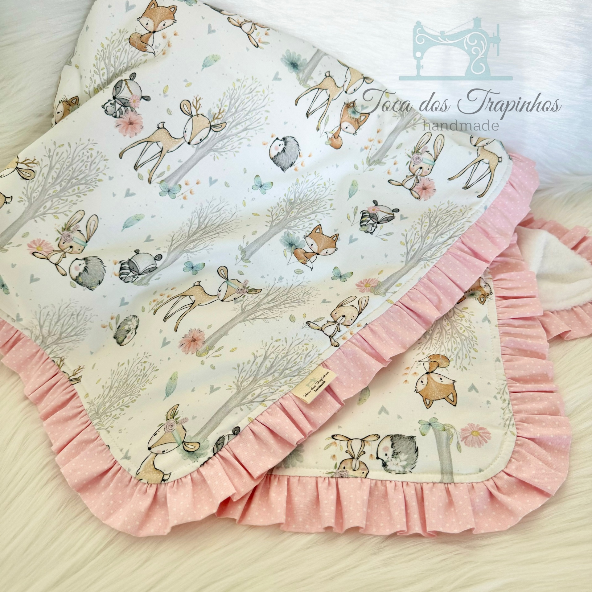 Cobertores infantis com padrão de animais e bordas rosa com pontos brancos.