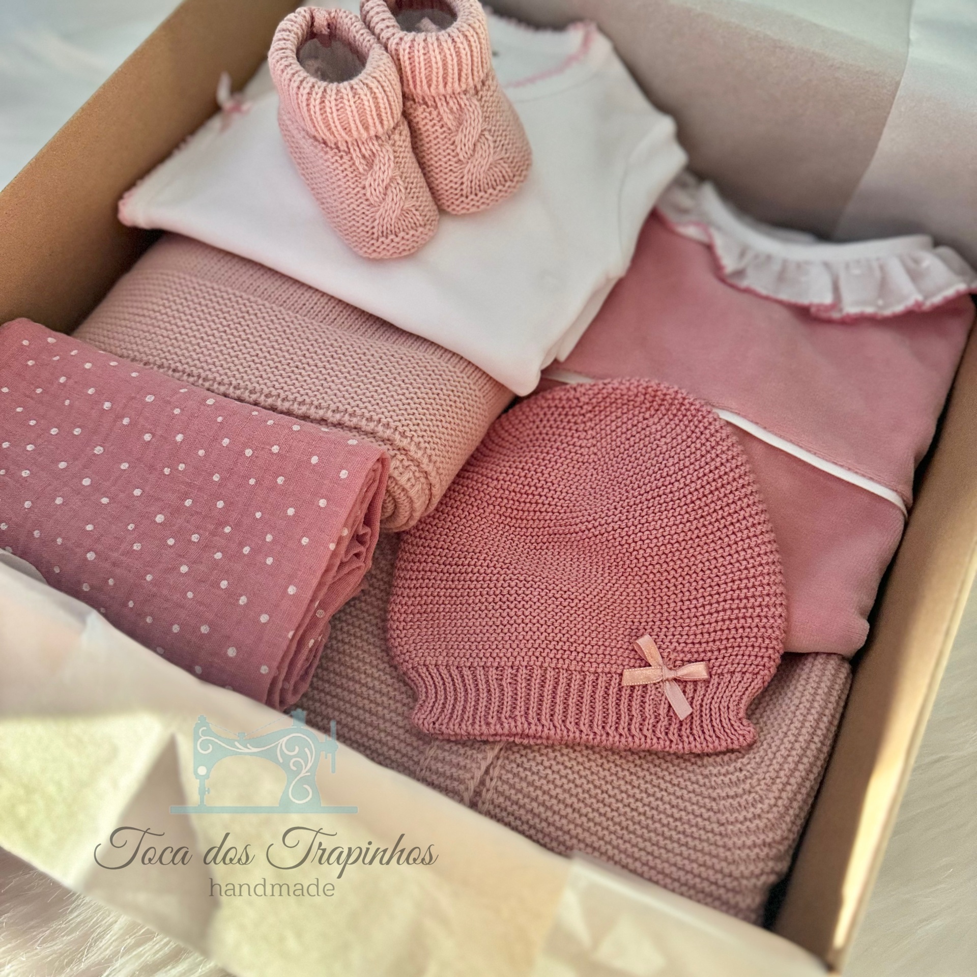Conjunto de roupa de bebé rosa com sapatinhos, manta, body, gorro e roupa numa caixa de cartão