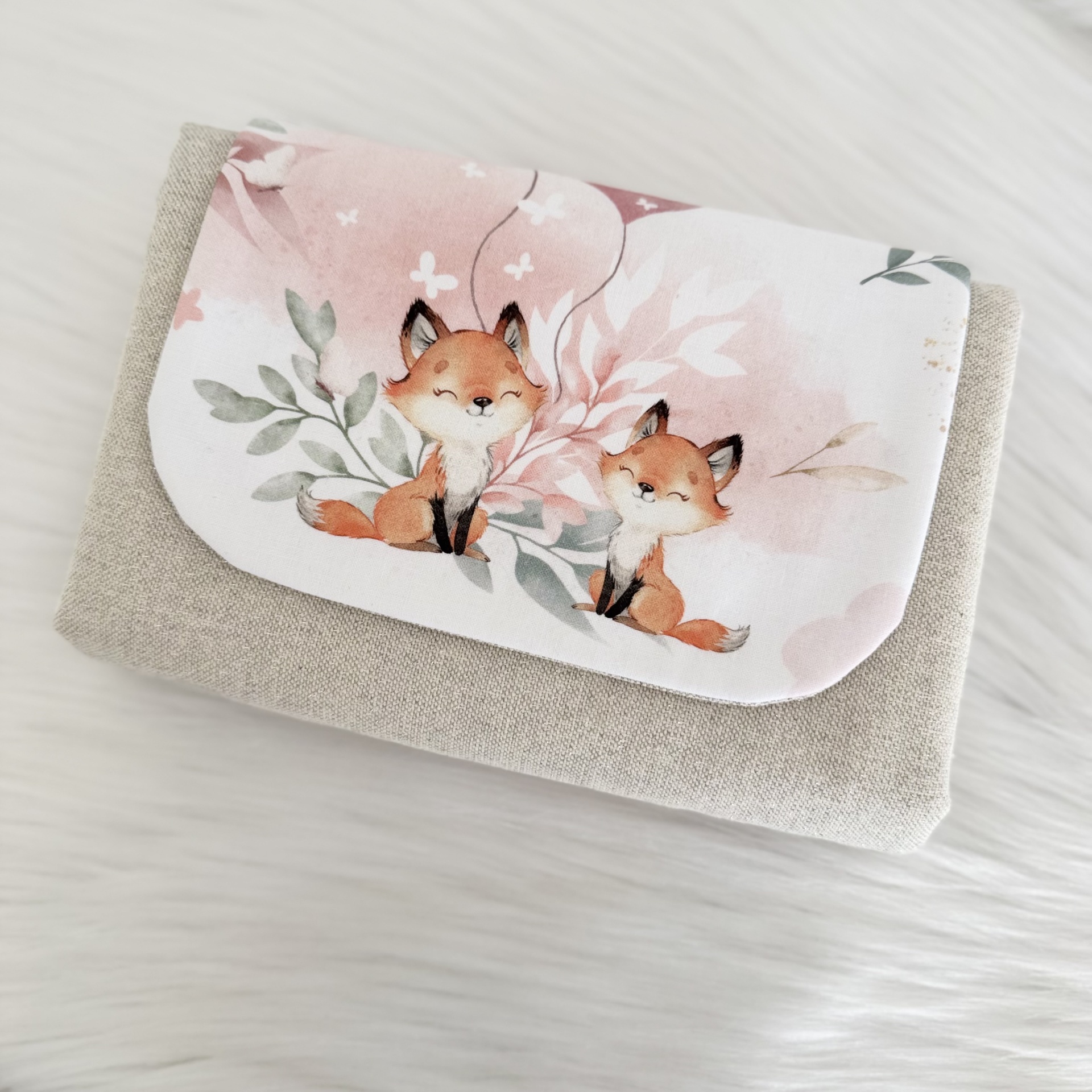 Carteira em tecido bege com aba branca decorada por ilustração de duas raposas e elementos florais
