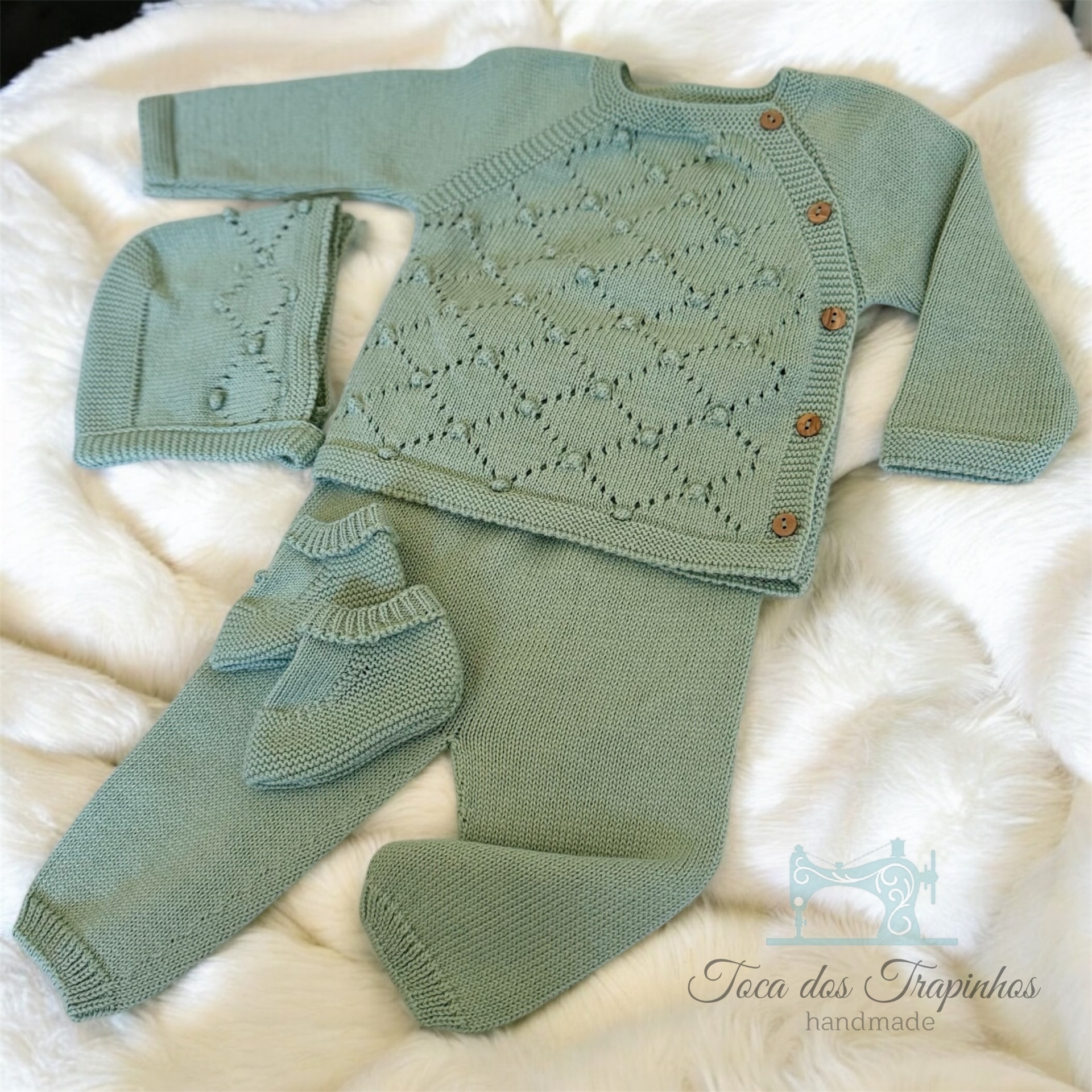 Conjunto de bebé em malha verde-água com camisola, calças, gorro e botinhas sobre tecido branco