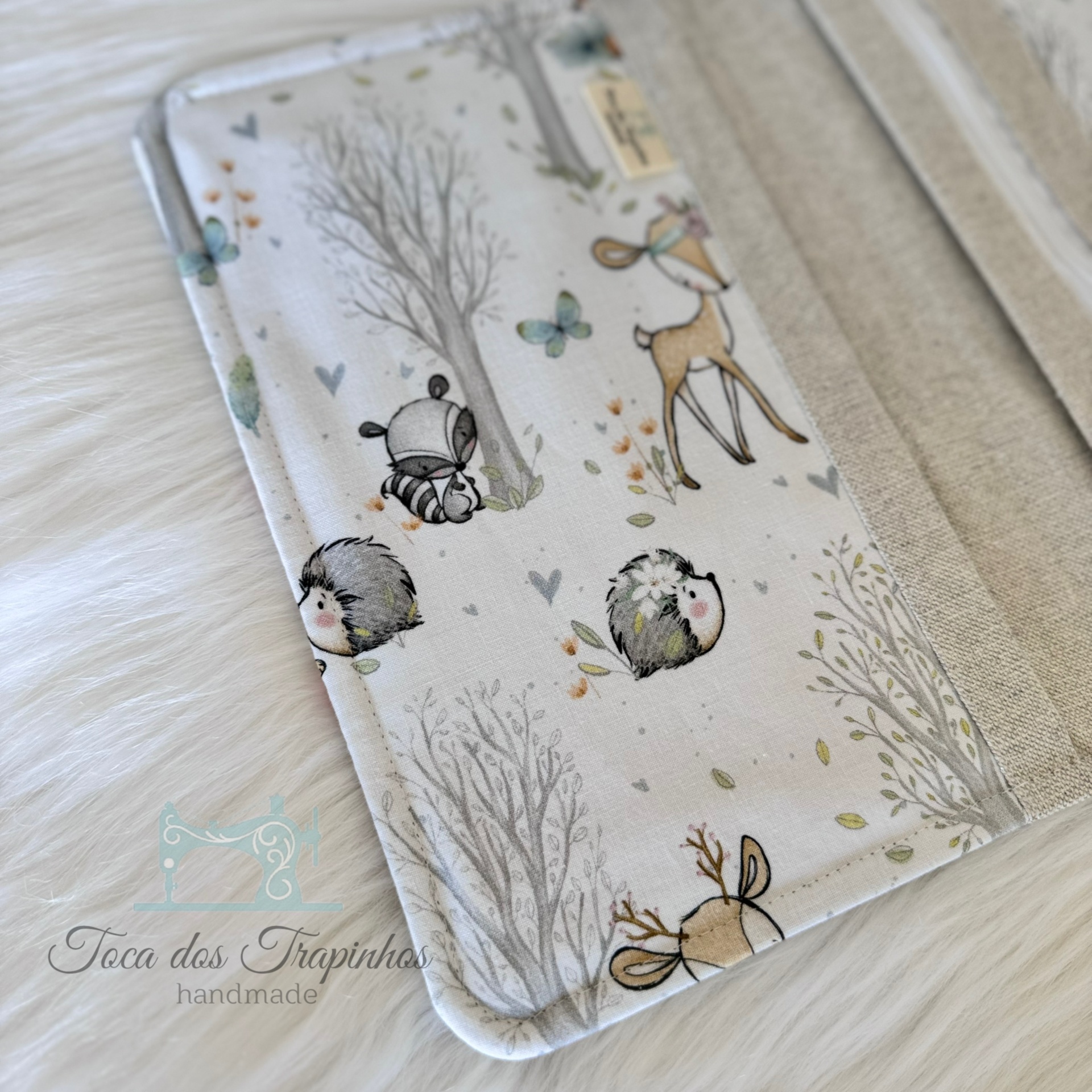 Capa almofadada com desenhos infantis de animais e árvores em tecido claro sobre fundo branco peludo