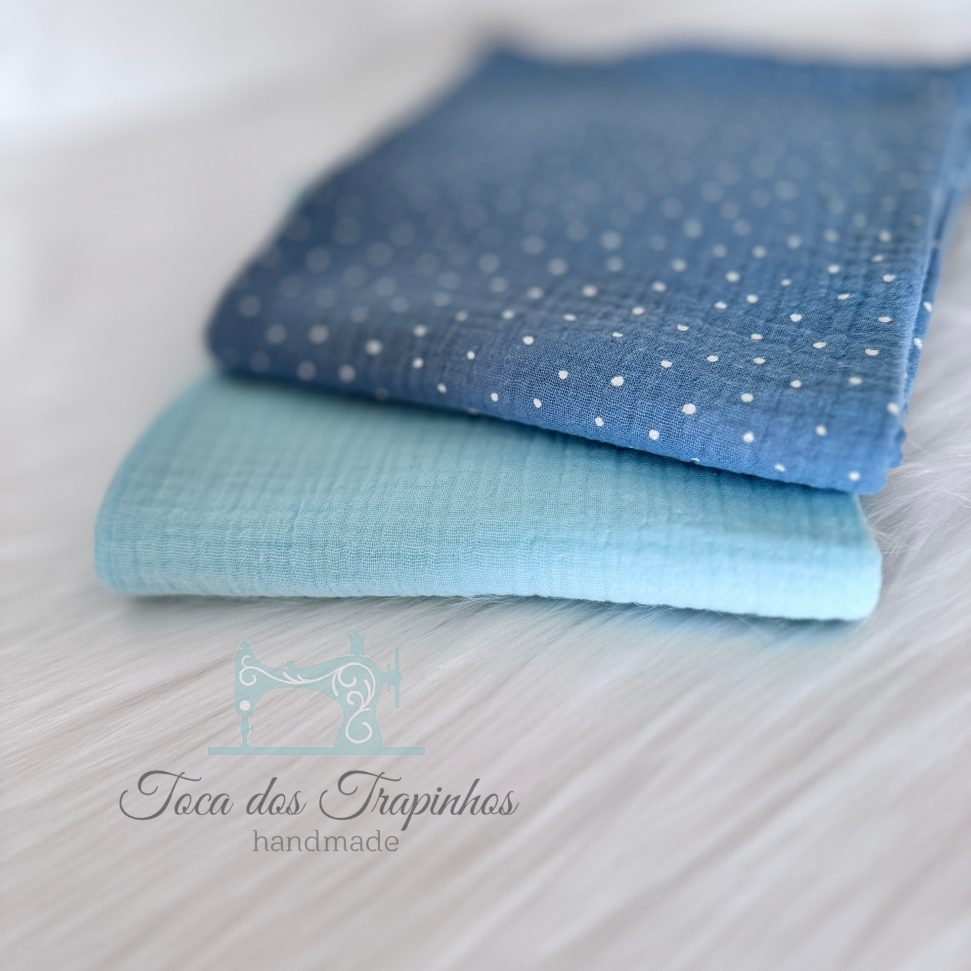 Duas toalhas azuis, uma lisa e outra com bolinhas brancas, sobre superfície branca felpuda
