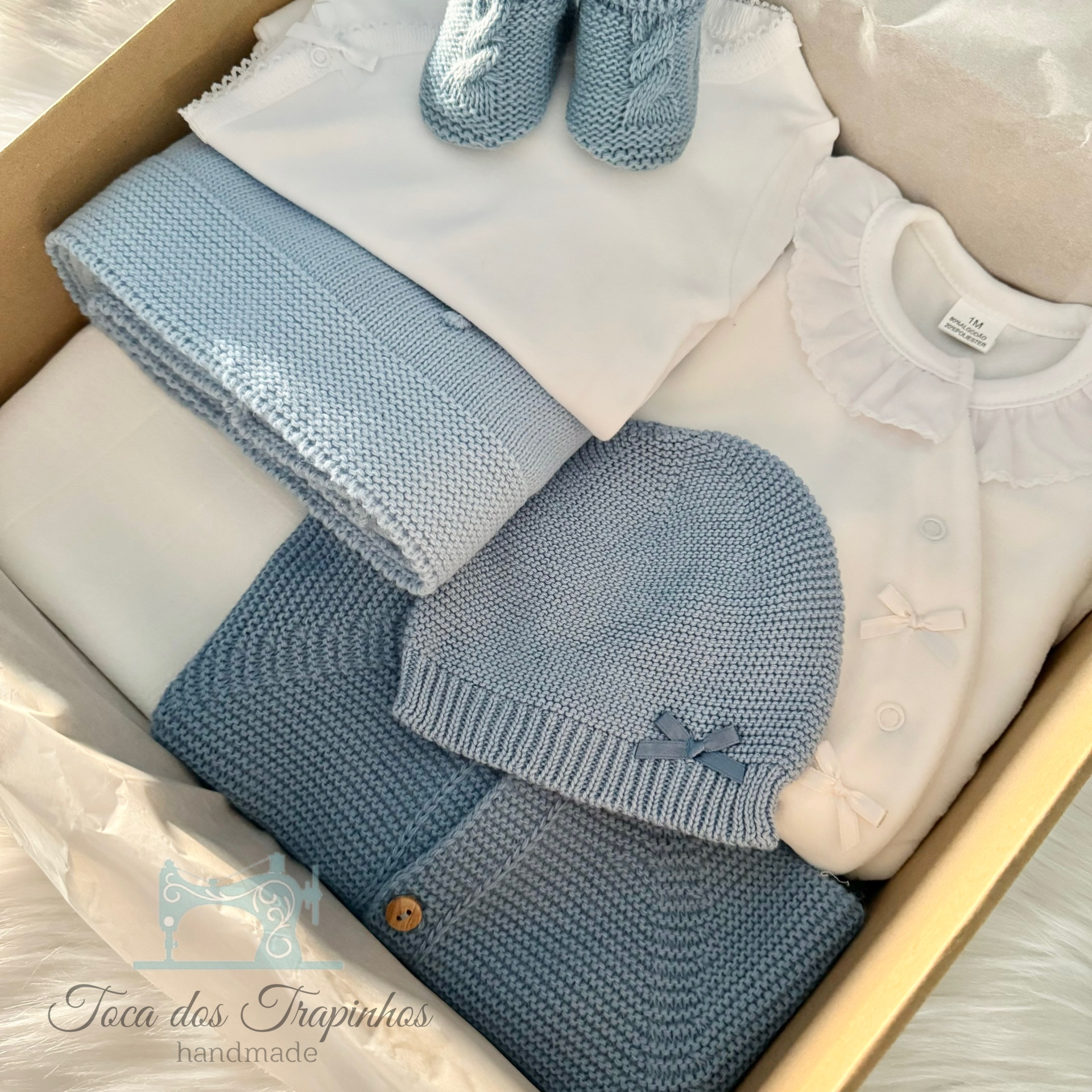Conjunto de roupa de bebé branco e azul dentro de caixa de papelão