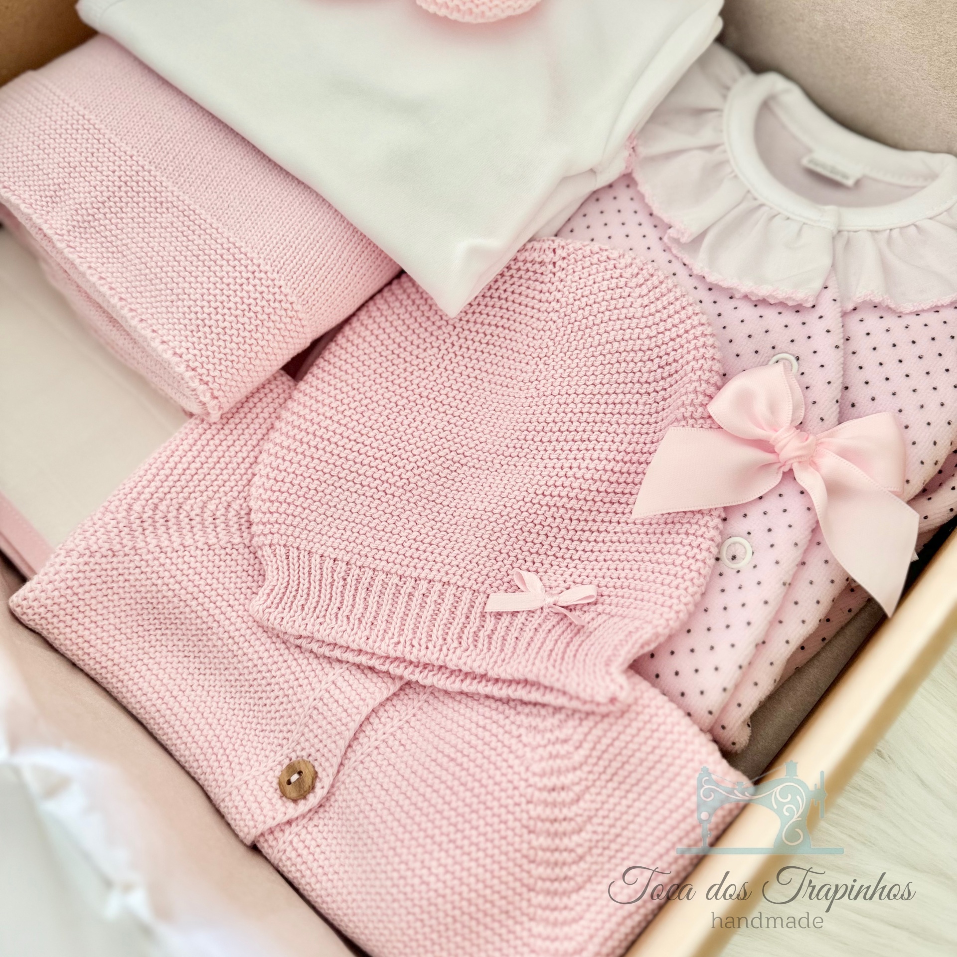 Roupas de bebé em tricot rosa e algodão branco numa caixa de madeira