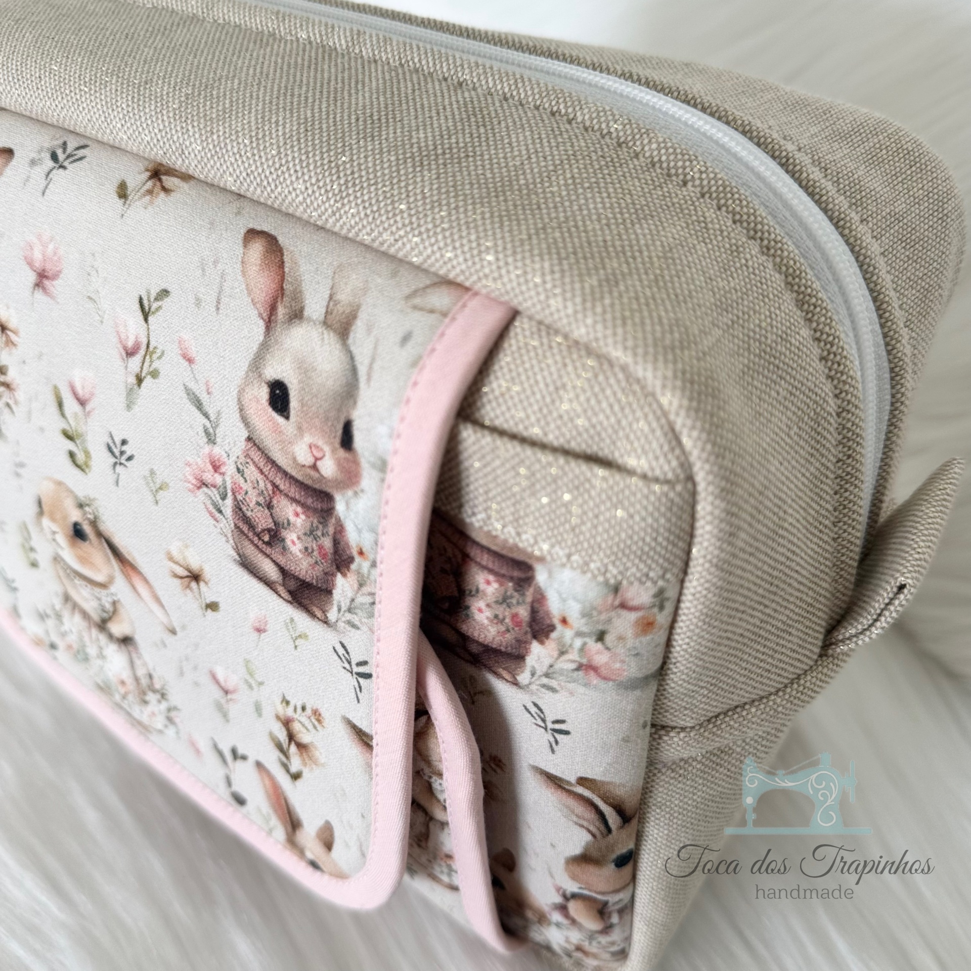 Necessaire bege com desenho de coelhinhos e flores, etiqueta Toca das Trapinhas
