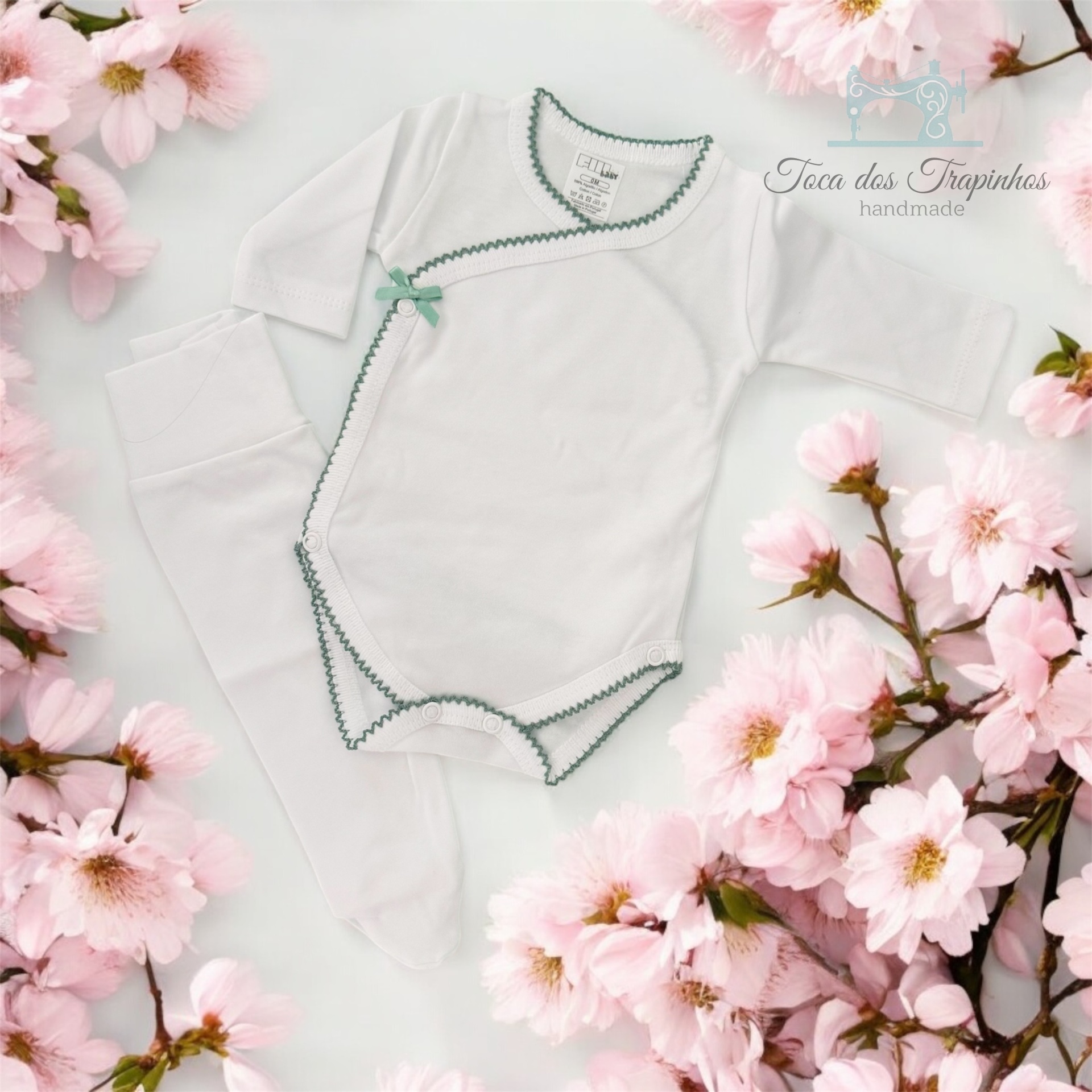 Conjunto de roupa de bebé branca com detalhes verdes e flores cor-de-rosa de fundo