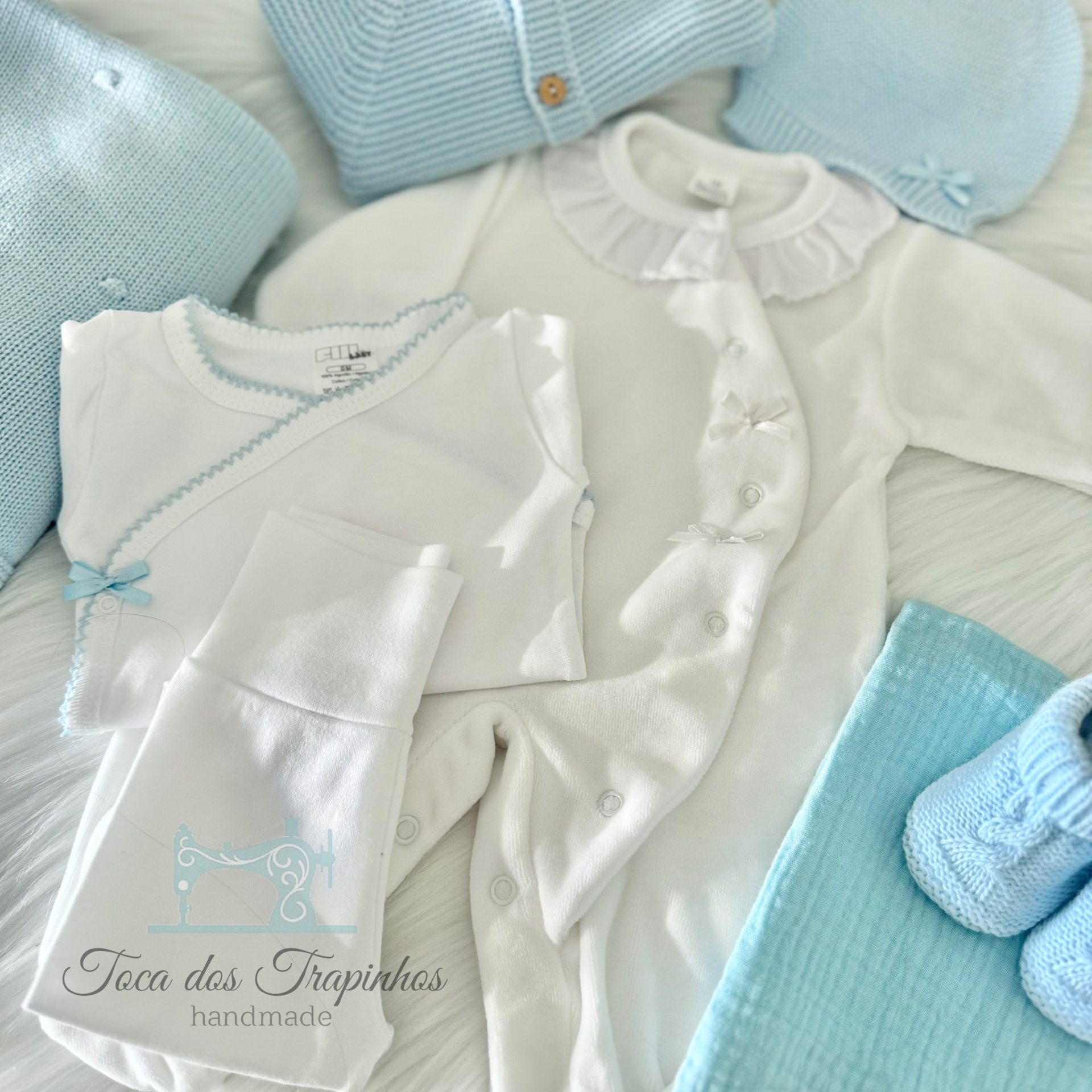 Conjunto de roupa de bebé branco e azul claro com vários acessórios em fundo branco