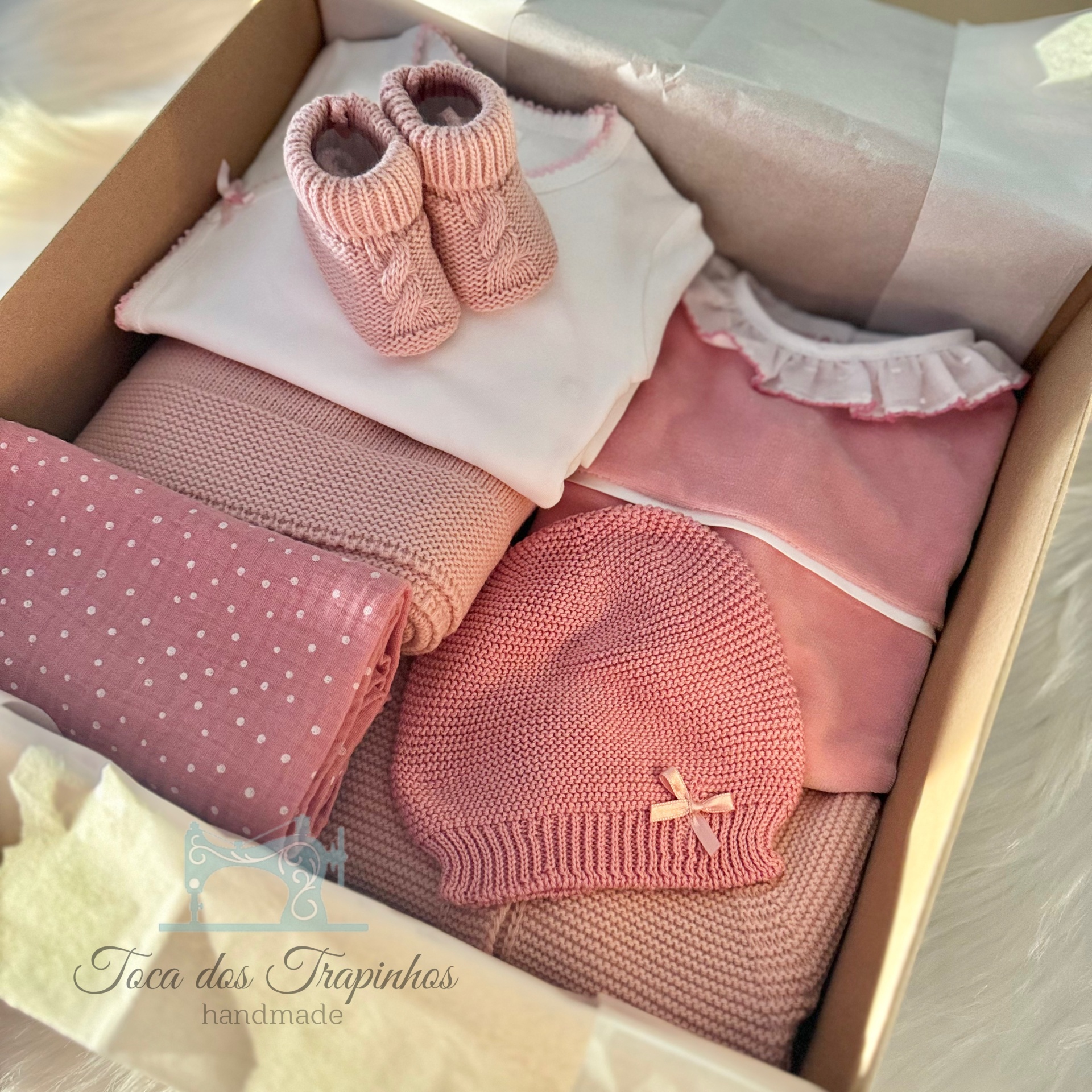 Conjunto de roupa e acessórios de bebê em rosa e branco dentro de caixa de presente