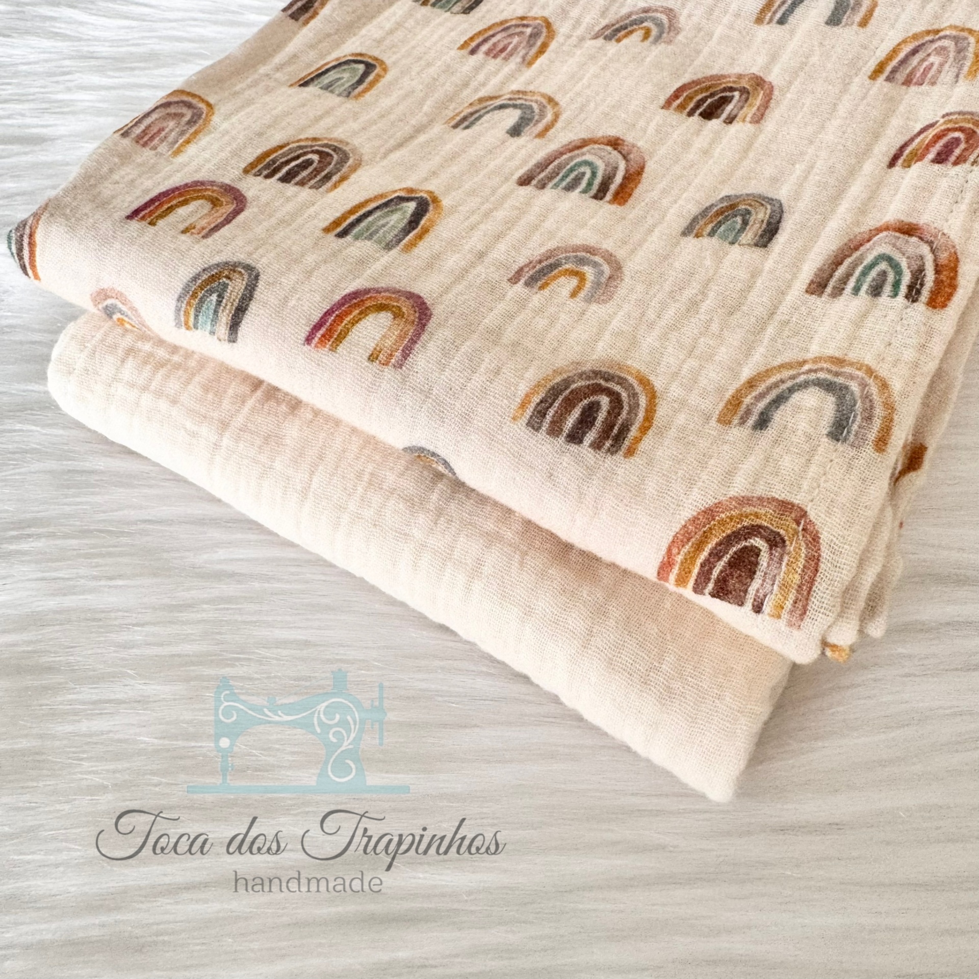 Duas mantas de algodão, uma com padrão de arcos-íris coloridos e outra lisa bege