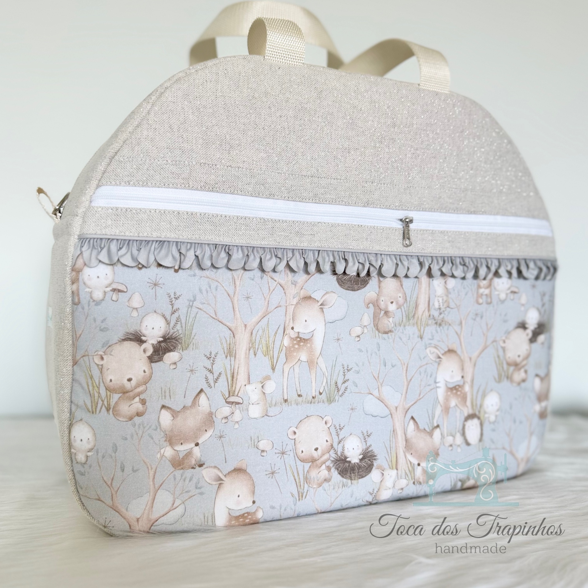 Mochila artesanal bege com padrão de animais da floresta e bolso frontal com fecho branco