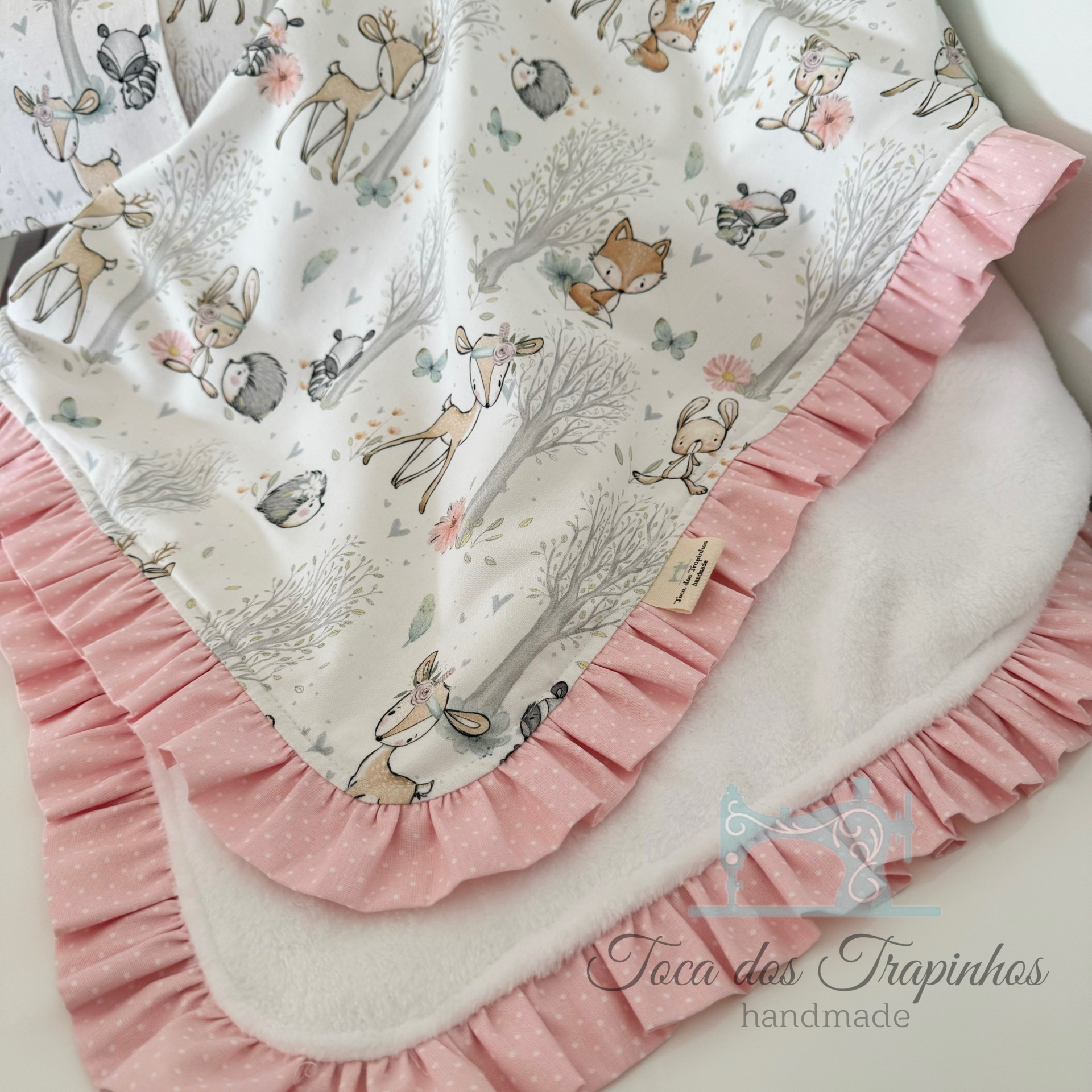 Manta branca com padrão de animais e borda rosa com bolinhas brancas