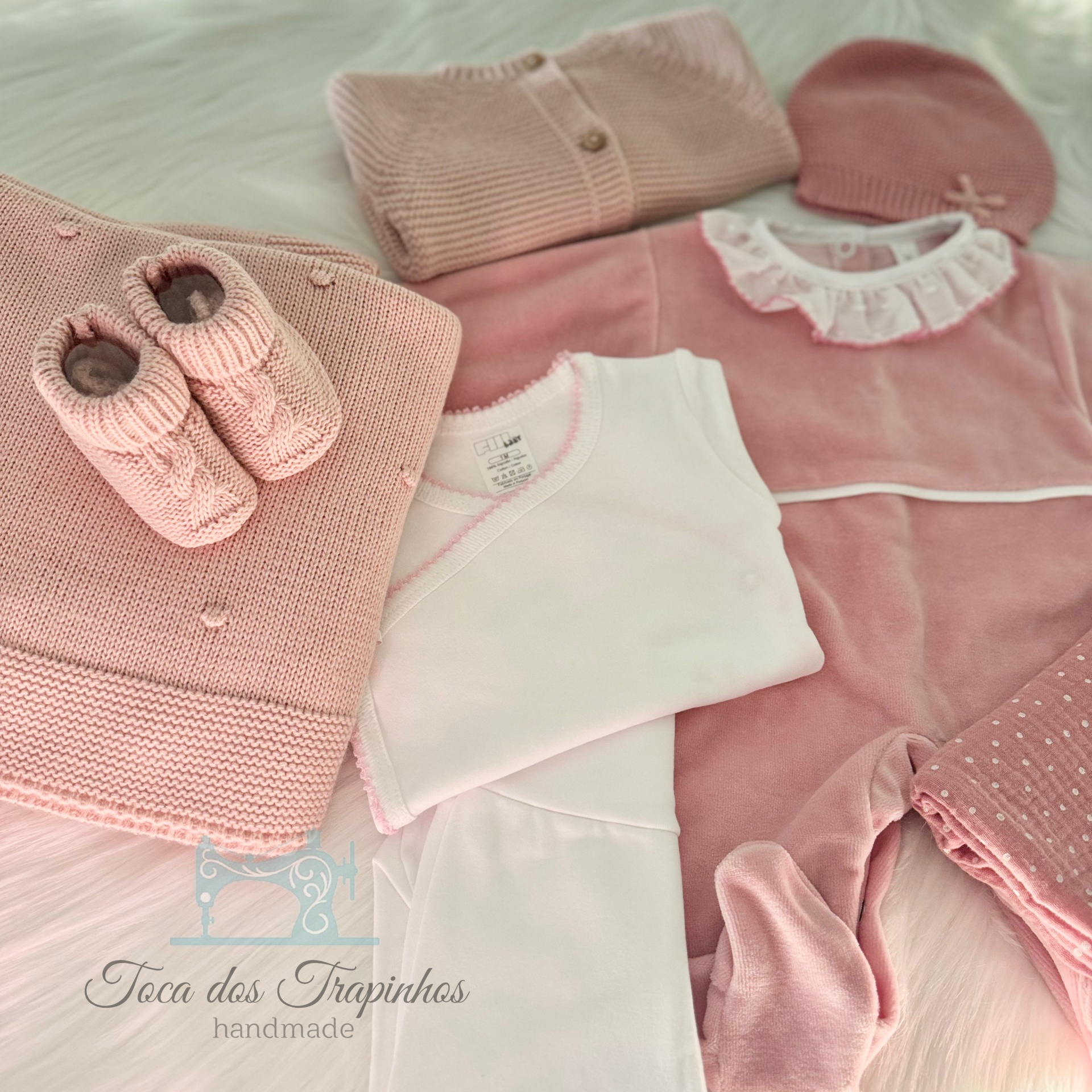 Roupas de bebé cor-de-rosa e branco, tecidos macios e malha, sobre superfície peluda branca