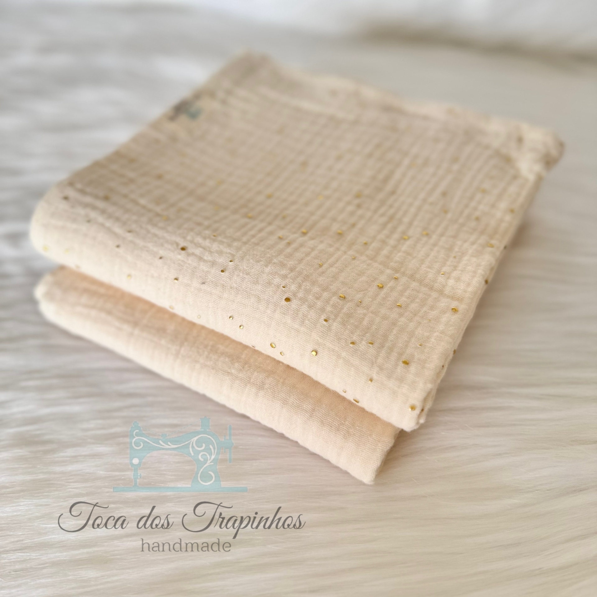 Duas mantas bege claro com textura macia e pontos dourados sobre fundo branco peludo