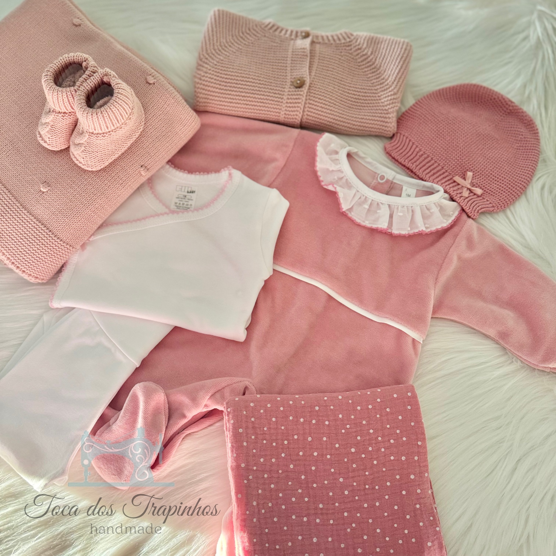 Conjunto de roupa de bebé cor-de-rosa com vários itens em superfície branca