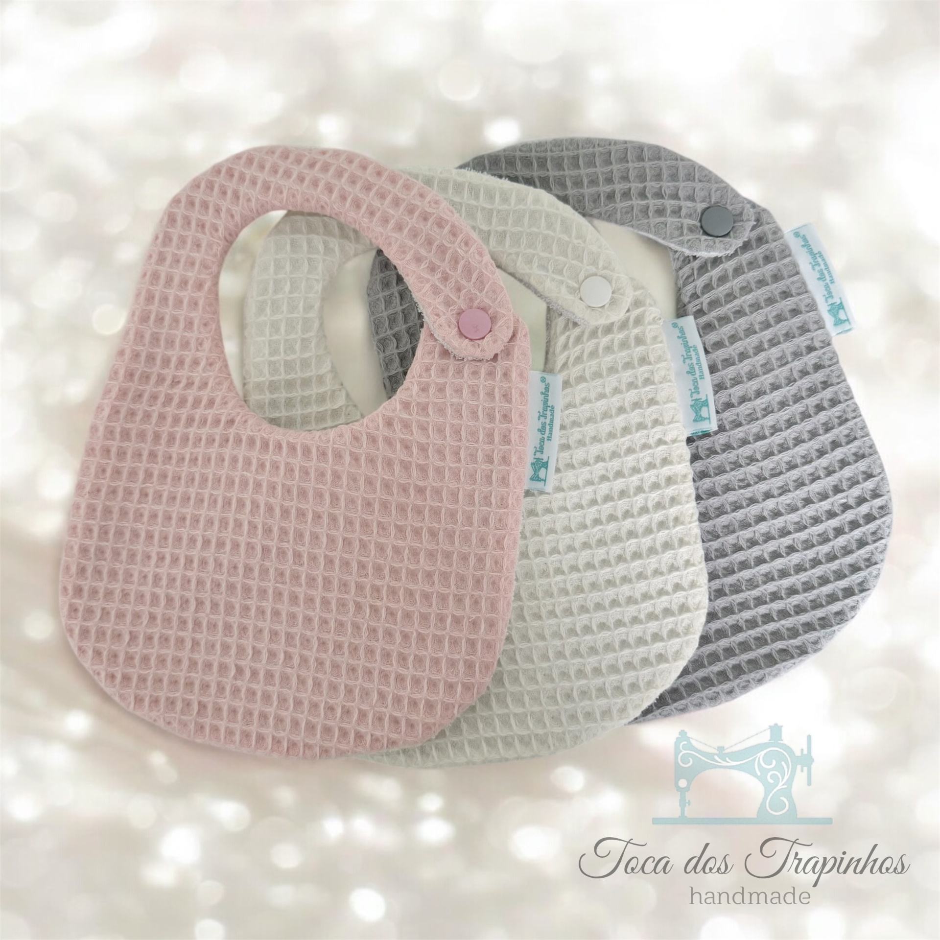 Três babetes de tecido texturizado nas cores rosa, bege e cinza