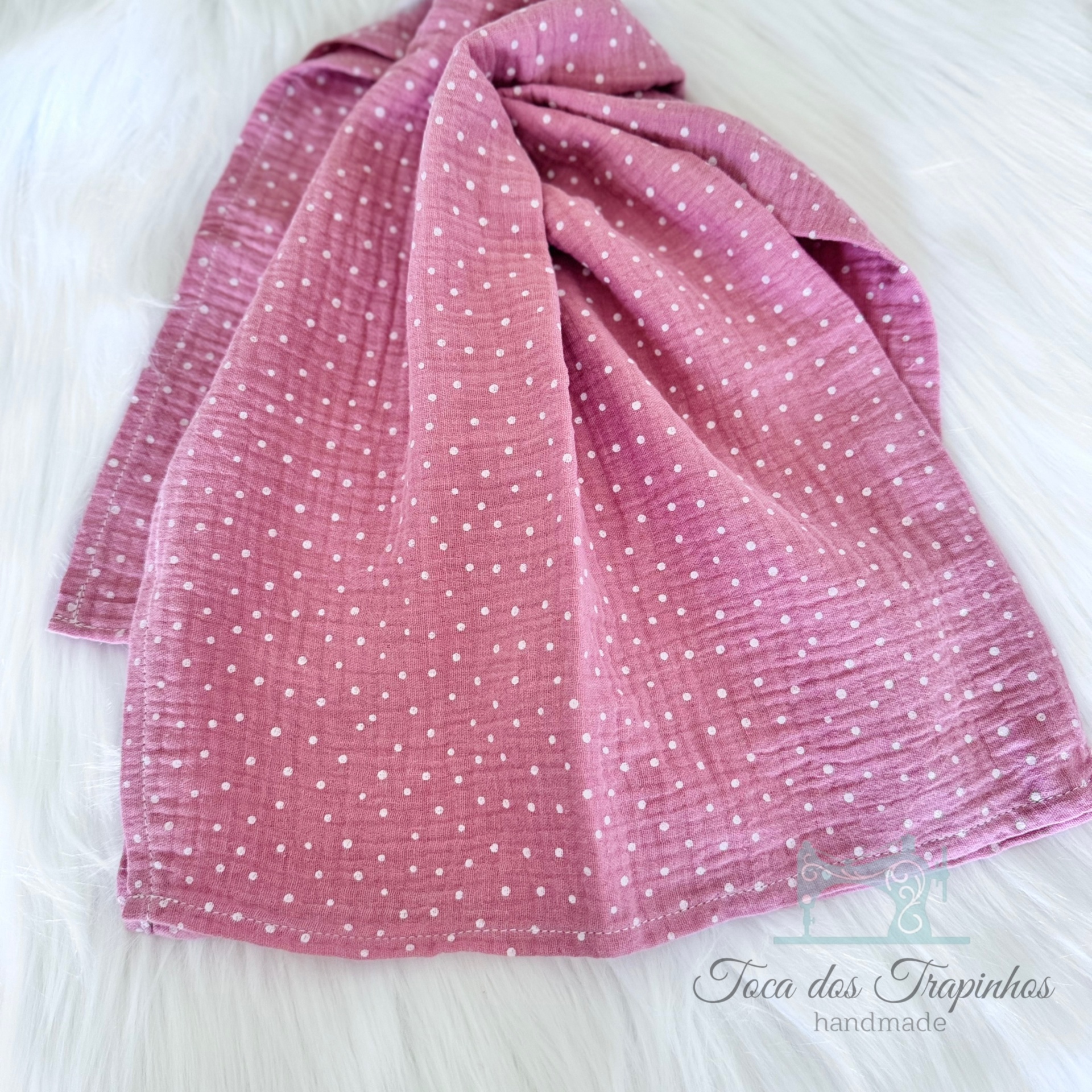 Lenço rosa com bolinhas brancas sobre superfície branca felpuda