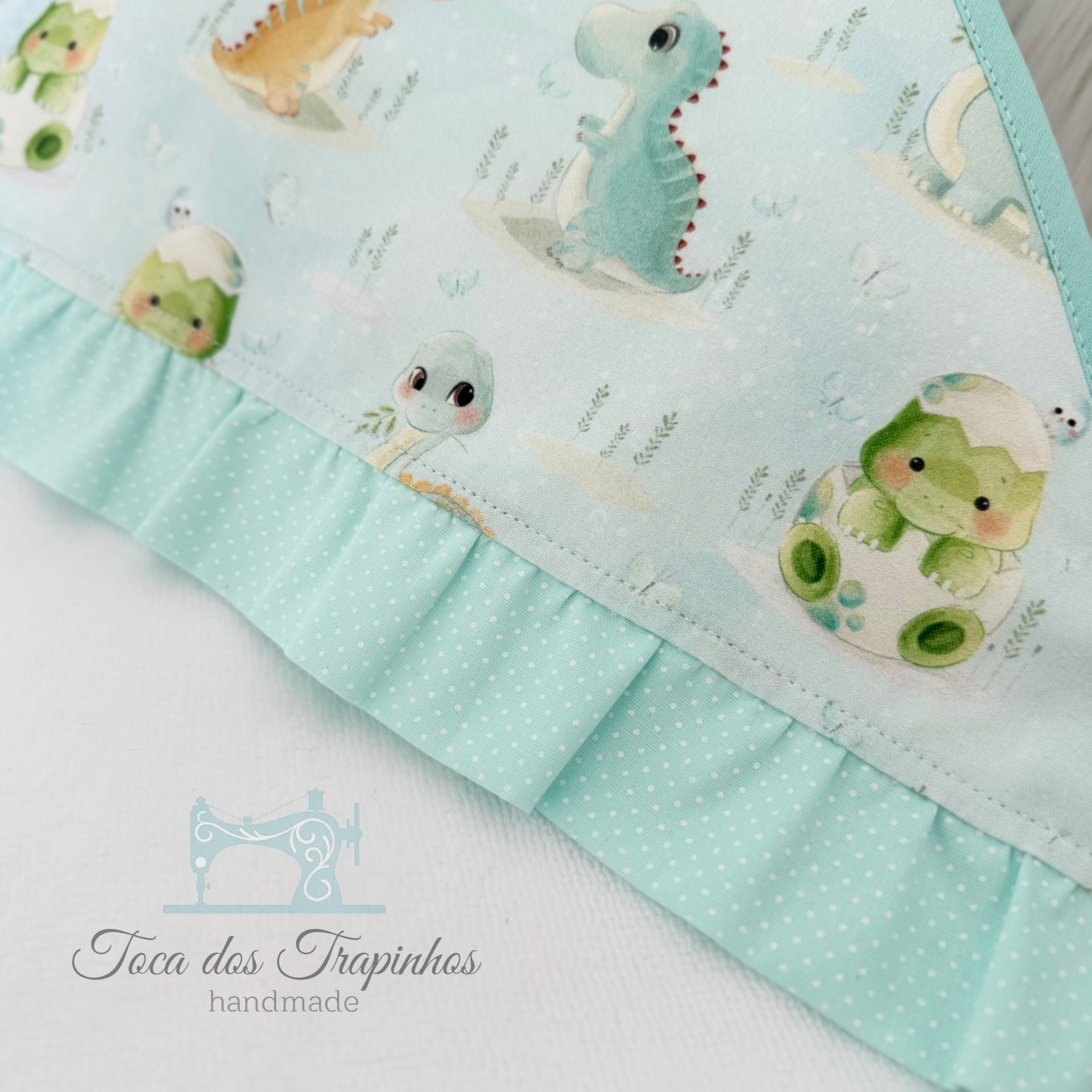 Tecido infantil azul com estampado de dinossauros e folho azul claro com pontos brancos.