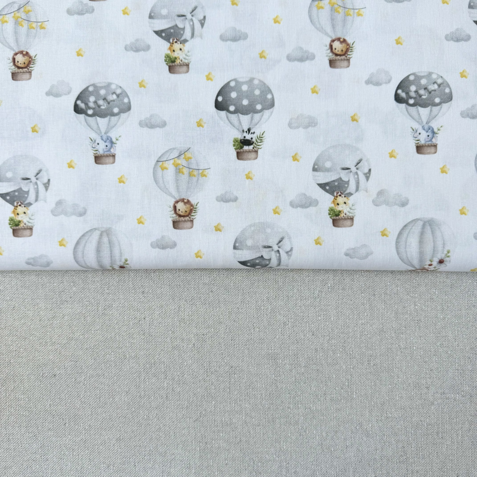 Tecido infantil com balões de ar quente e animais em fundo branco e tecido cinza abaixo