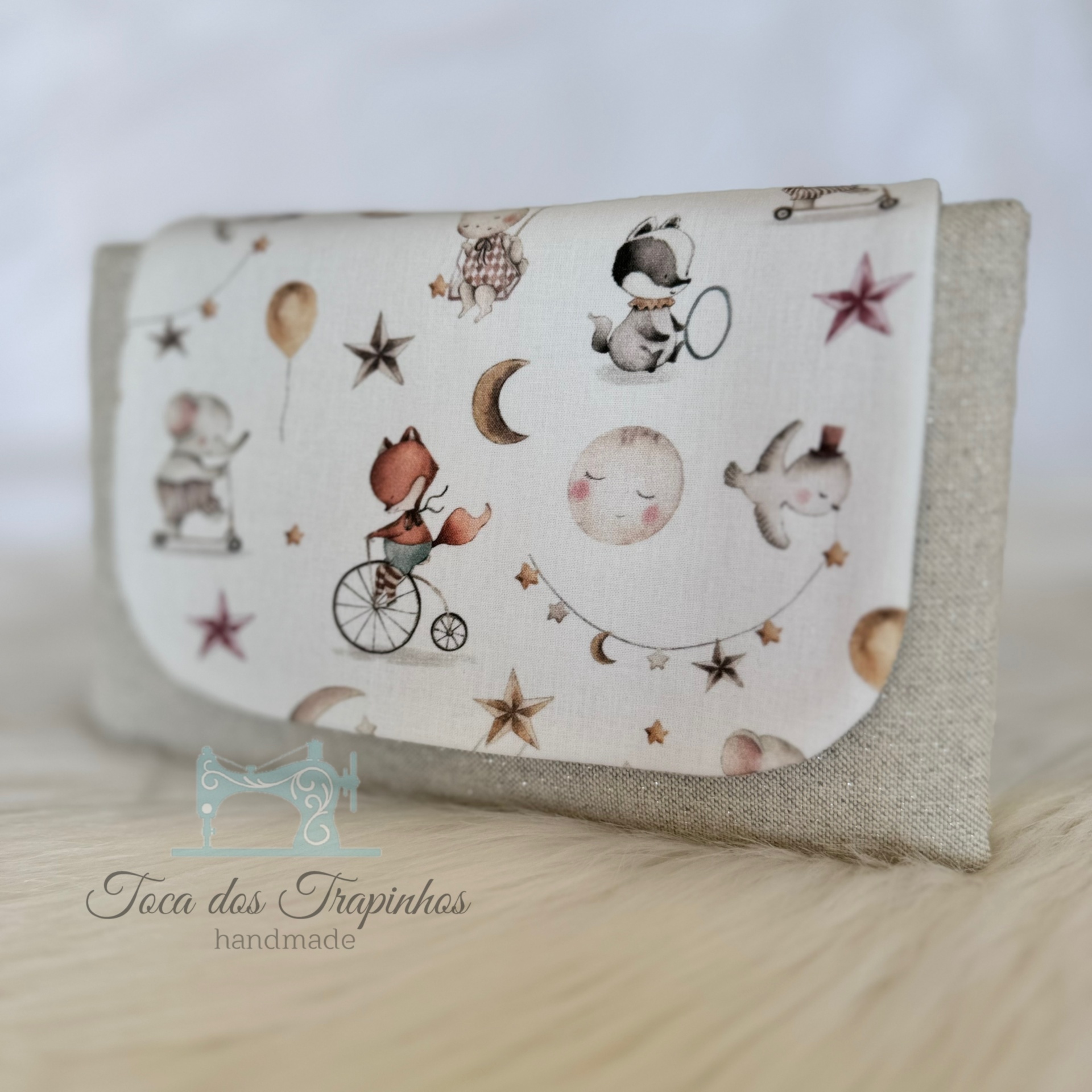 Carteira pequena com tecido bege e aba com padrão de animais e estrelas em tons pastel.