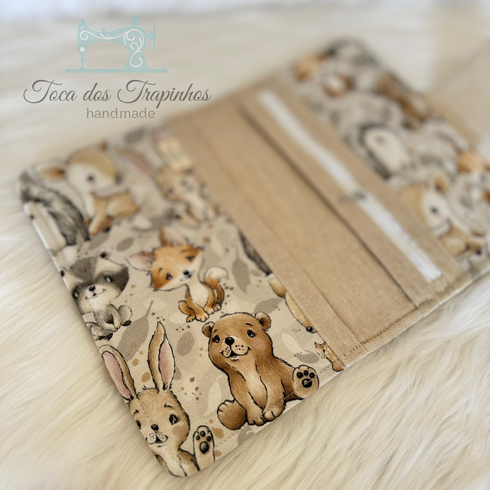 Carteira ou porta-cartões com padrão de animais em tons beige e castanho colocada sobre superfície branca de pelo.