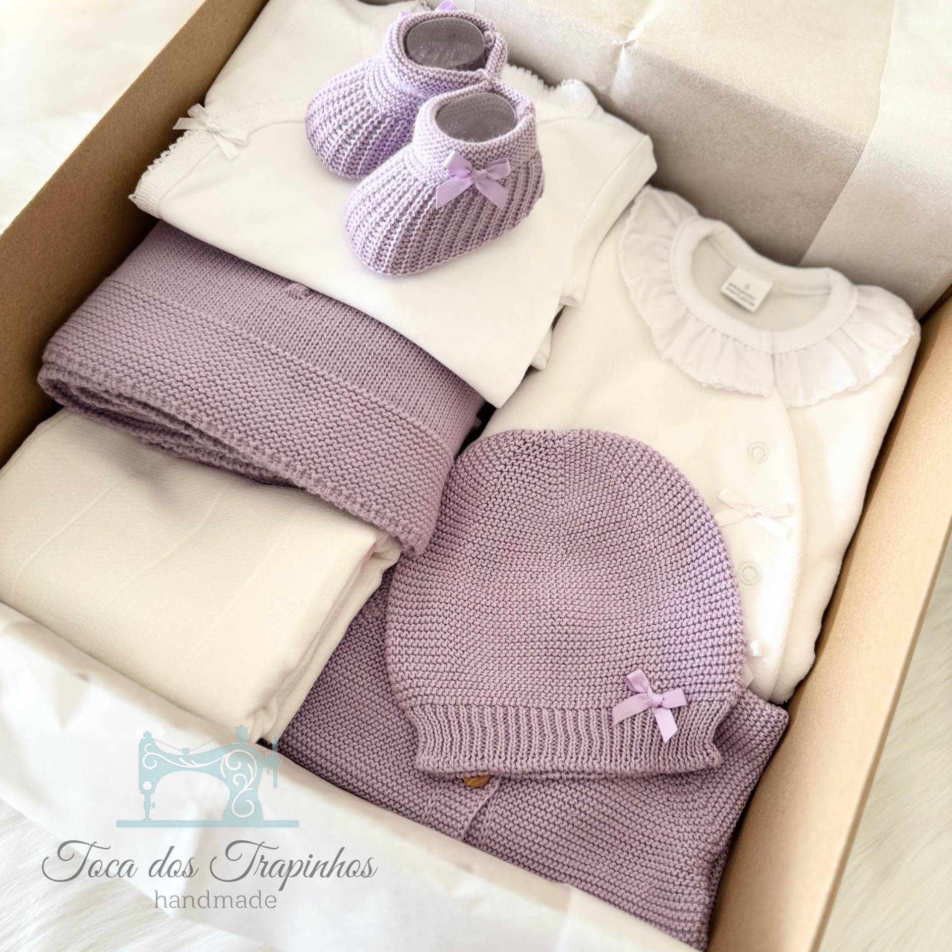 Conjunto de bebé lilás e branco com sapatinhos, gorro e cobertor tricotados em caixa