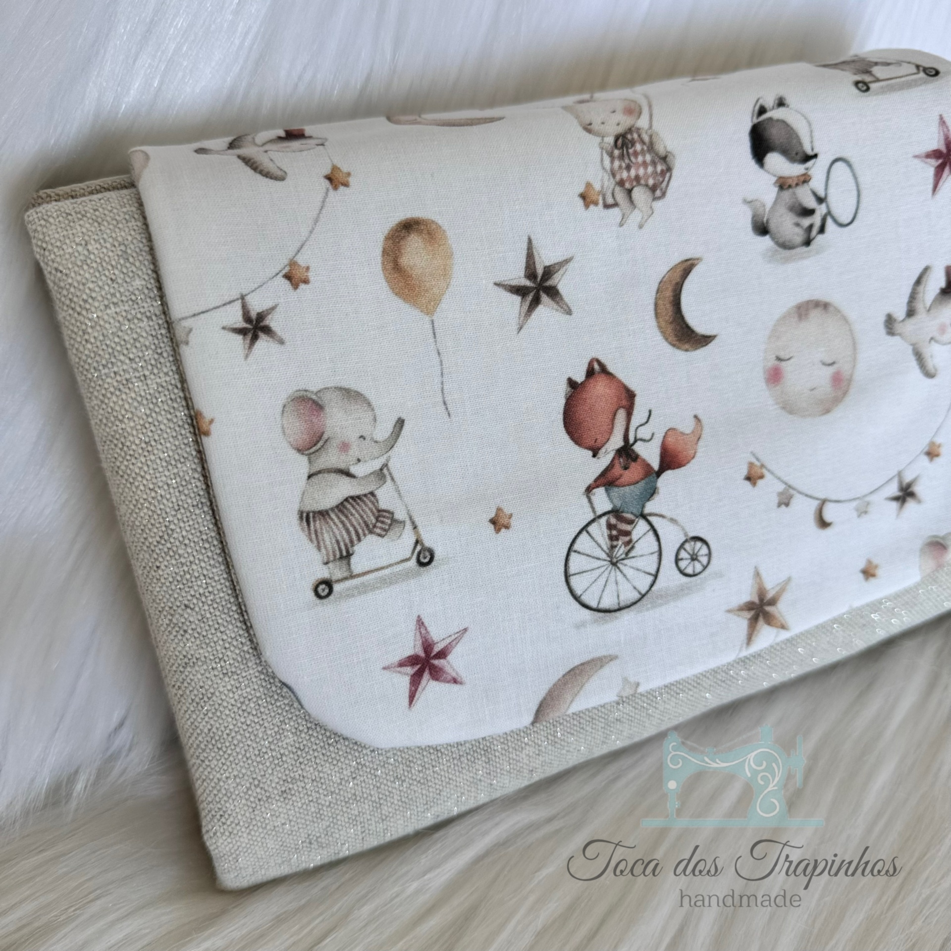 Carteira de tecido bege claro com aba branca decorada com desenhos infantis de animais e elementos celestiais