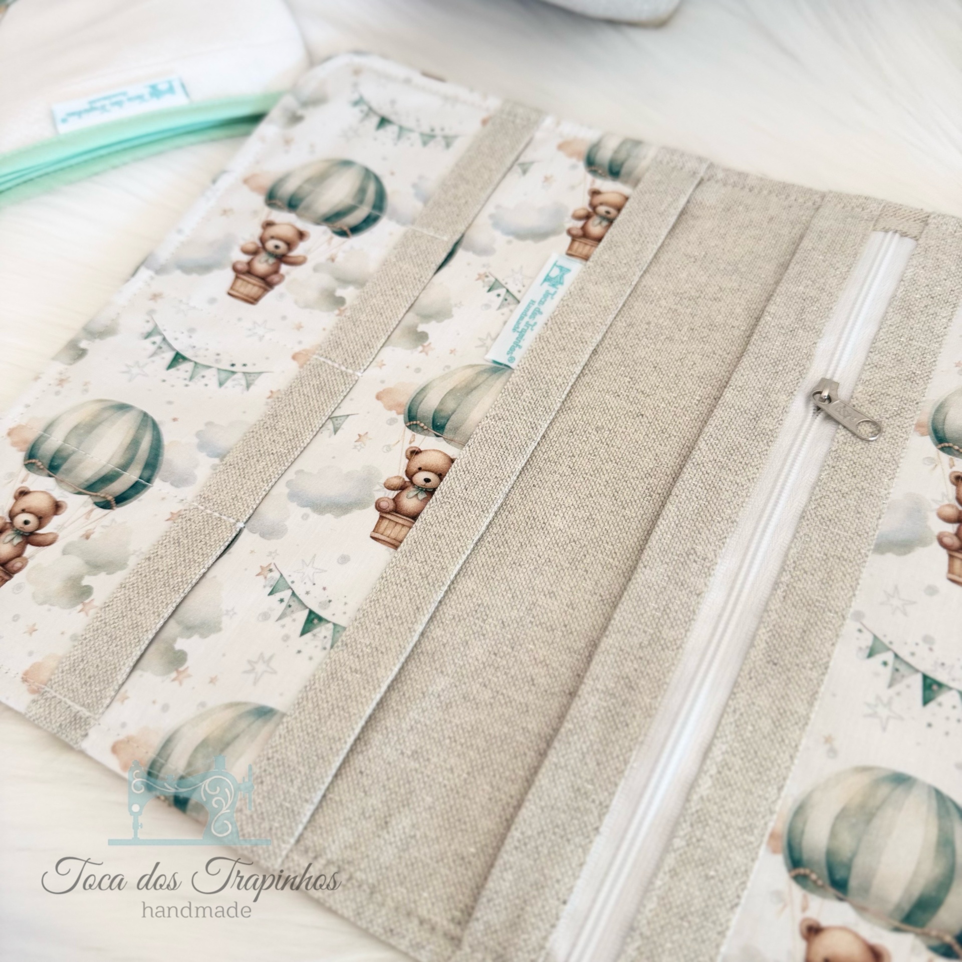 Estojo de tecido com estampa de balões e ursinhos, fecho de correr branco e detalhes beges.