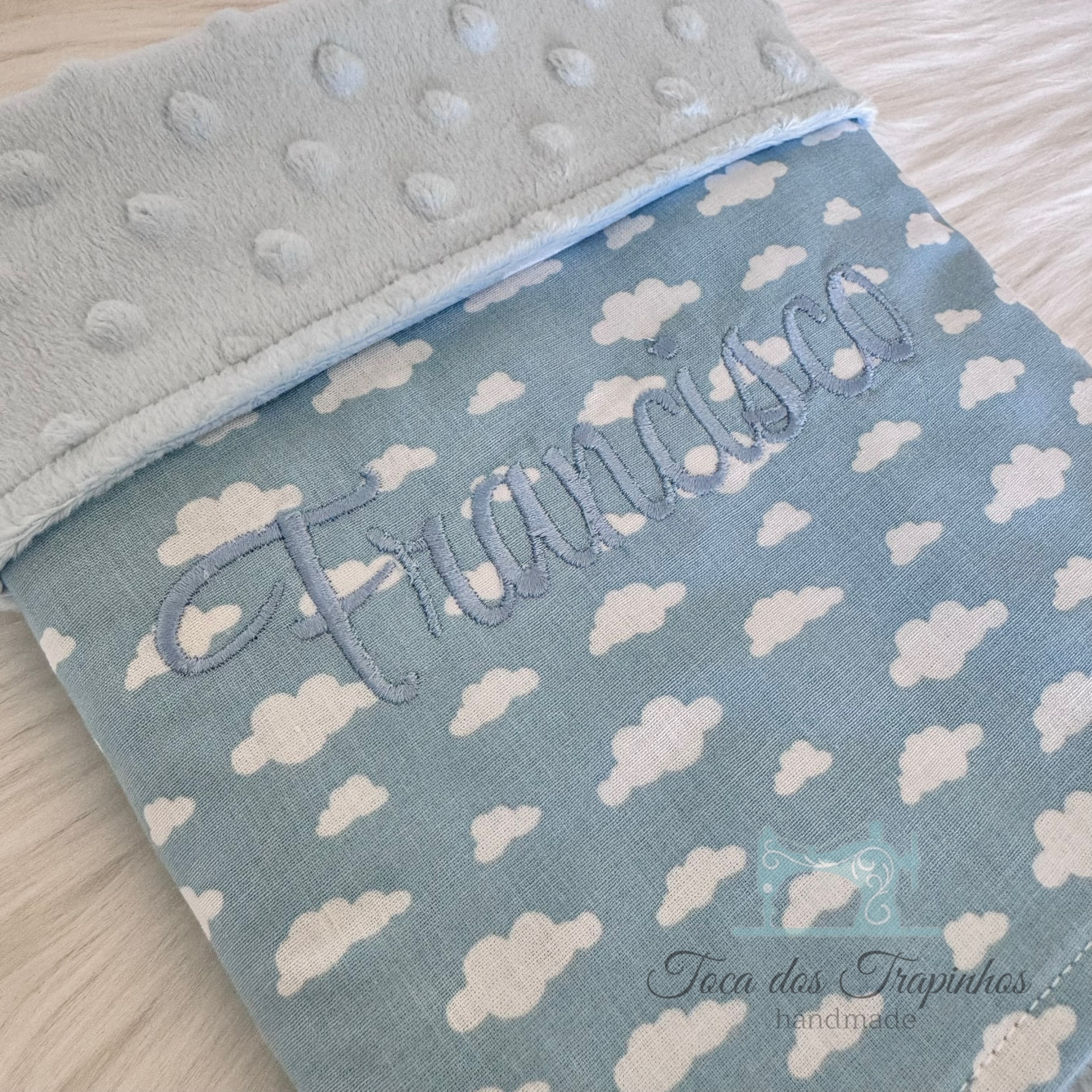 Manta azul com nuvens brancas e bordado com o nome Francisco
