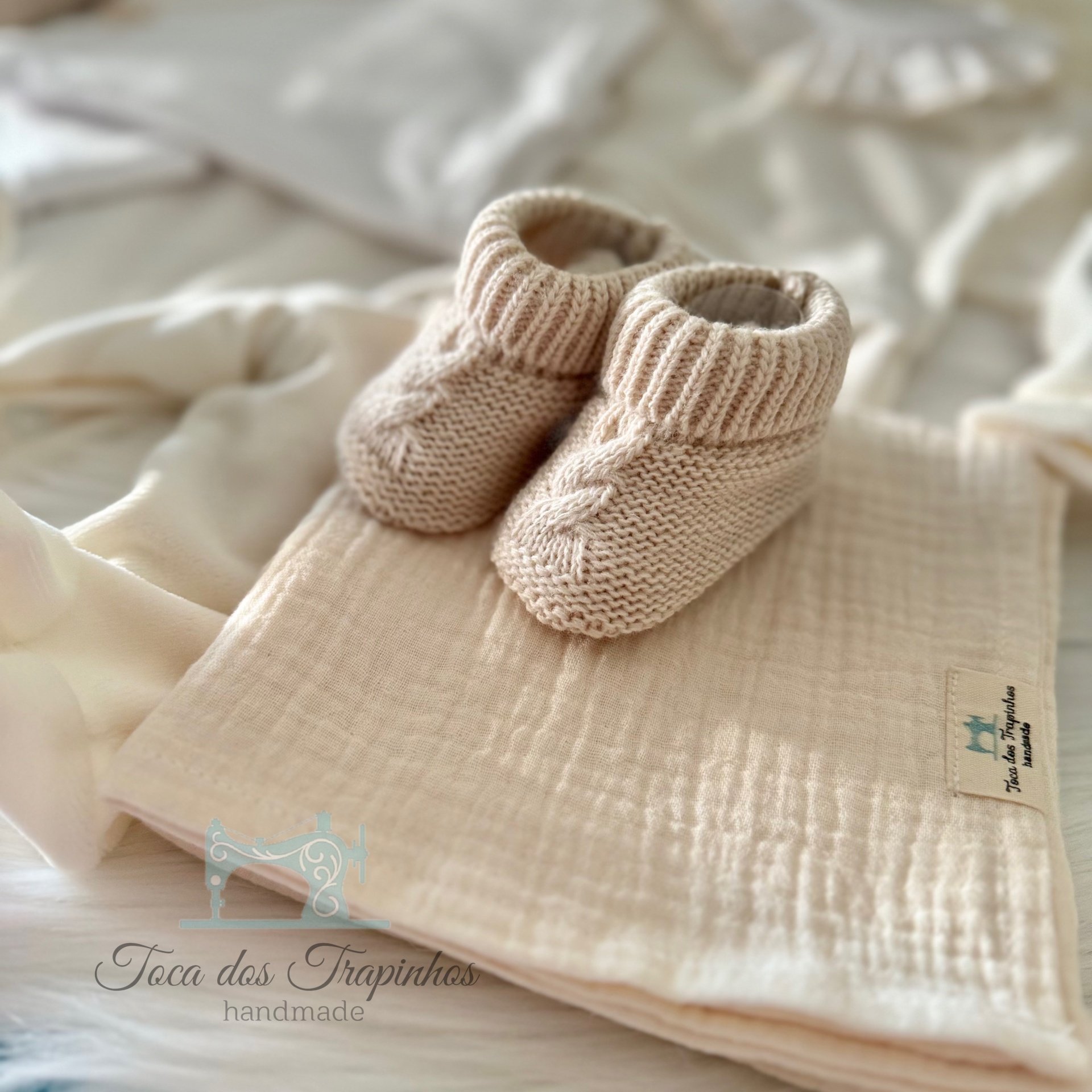 Botins de malha bege para bebé sobre tecido bege com etiqueta