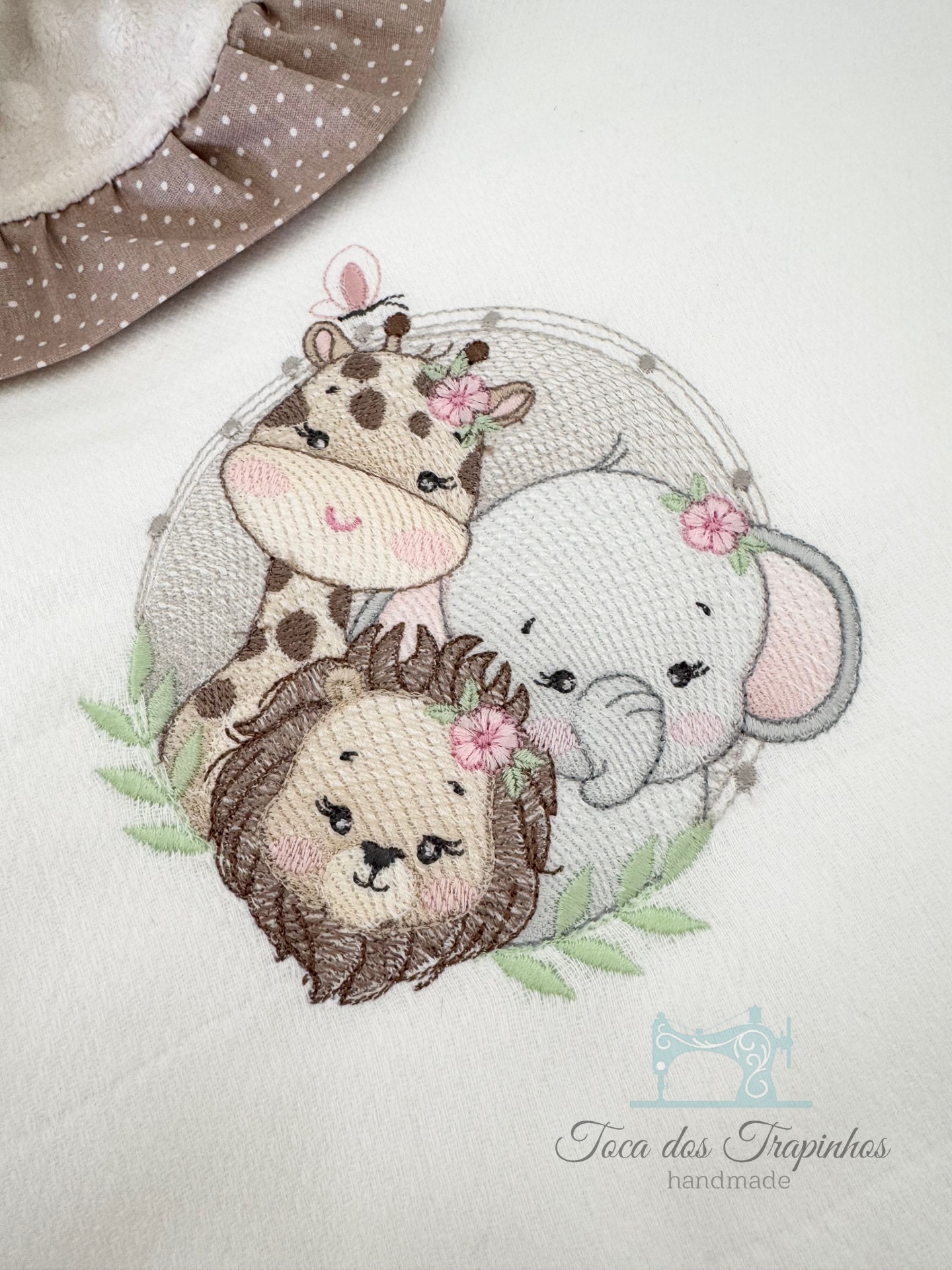 Bordado de girafa, elefante e leão em tecido branco com texto 'Toça das Trapinhos handmade'.