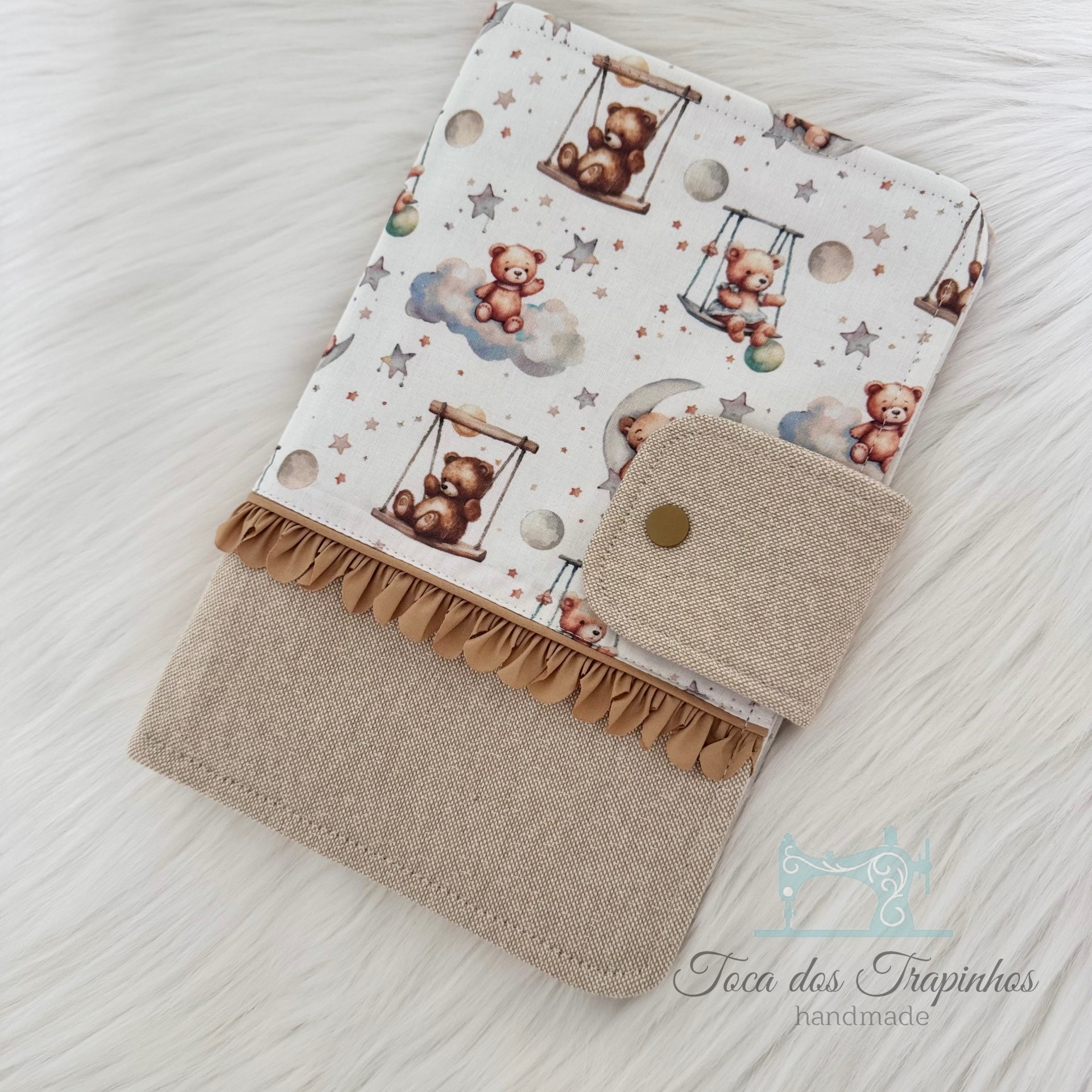 Capa de tecido com padrão de ursinhos e fecho bege sobre superfície branca macia