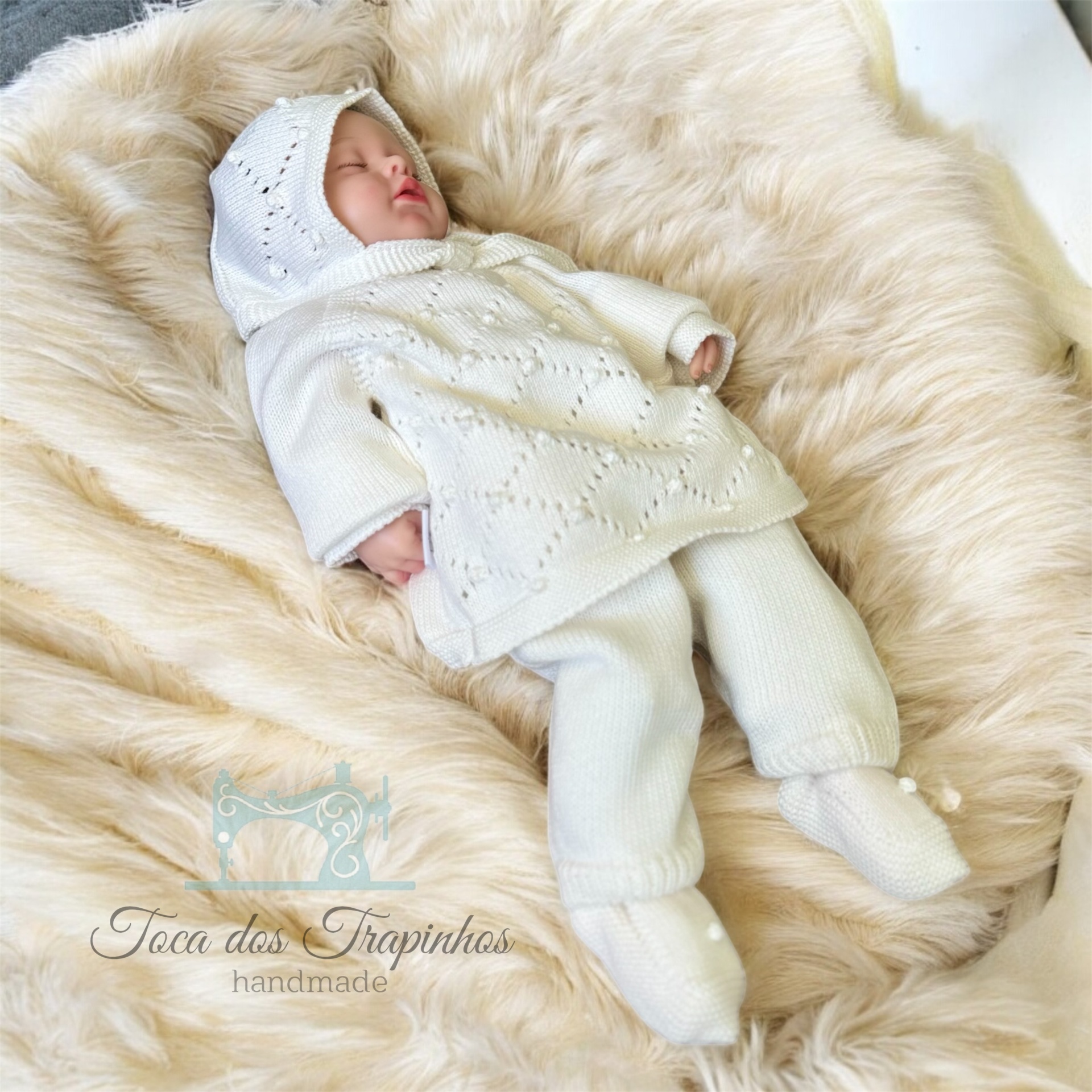 Conjunto de bebé de malha branca com vestido, calças e capuz sobre superfície felpuda bege