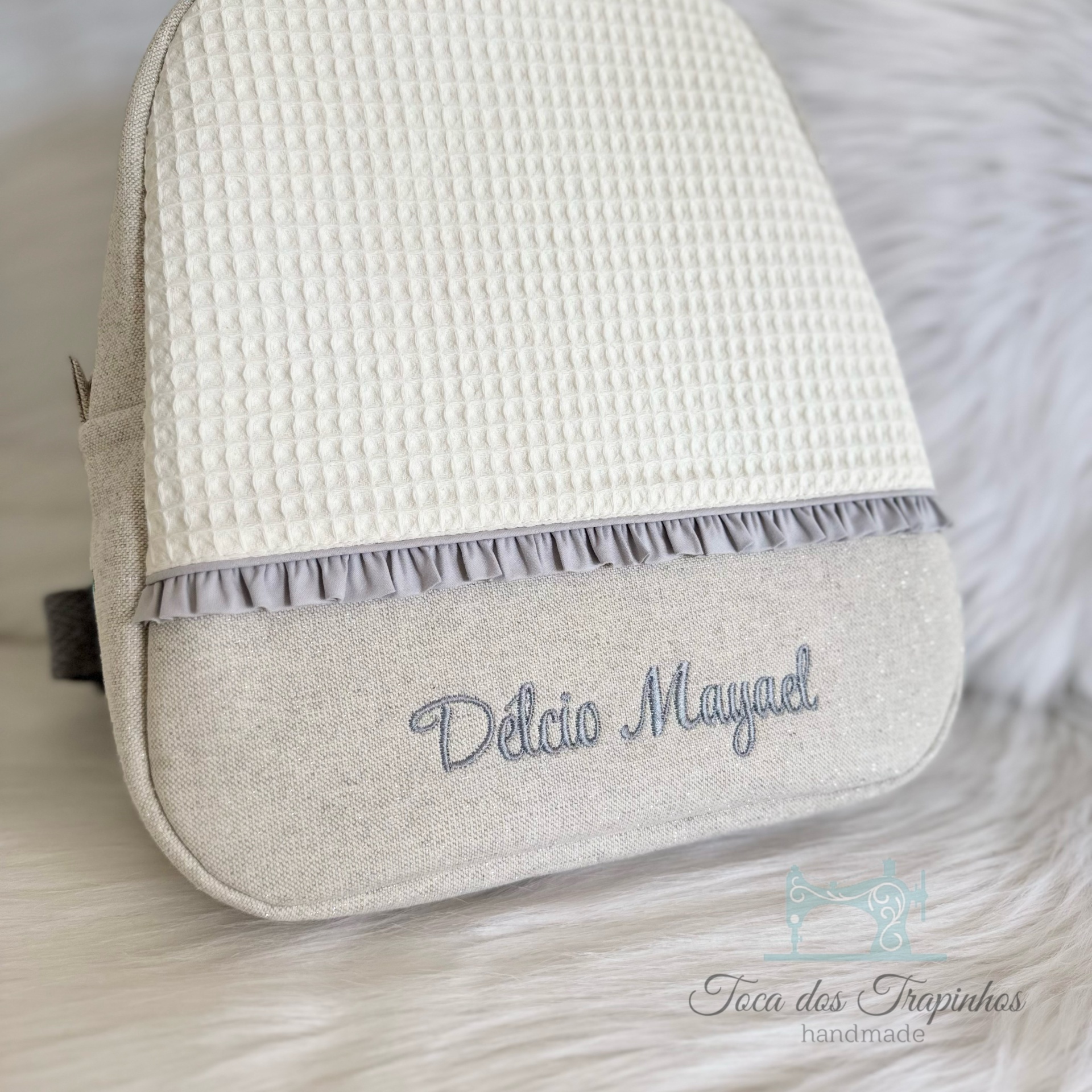 Mochila bege com flap branco quadriculado, folho cinzento e bordado Delcio Mayal