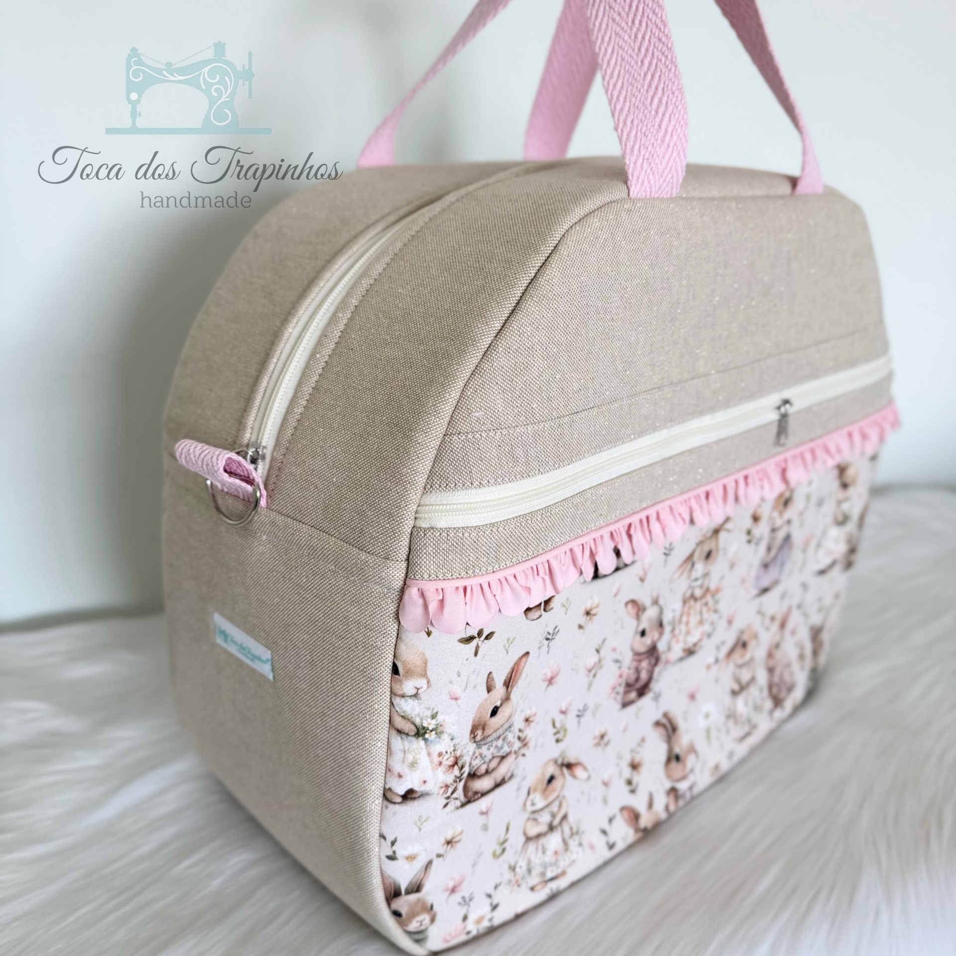 Mala bege artesanal com alças rosa e bolso frontal com padrão de coelhos.