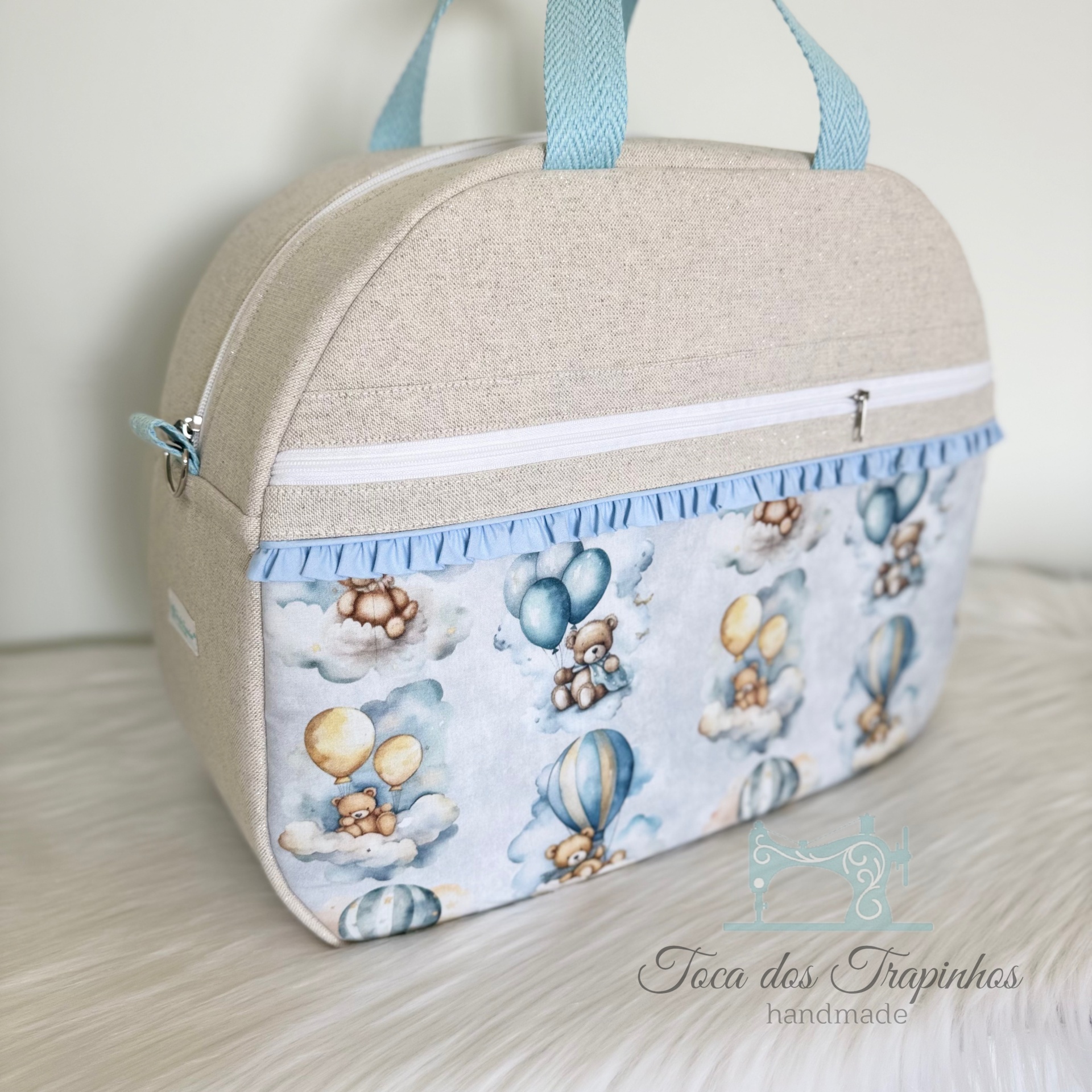 Mala bege para bebé com bolsos estampados de ursinhos e balões, com alças azuis e folhos azuis claro