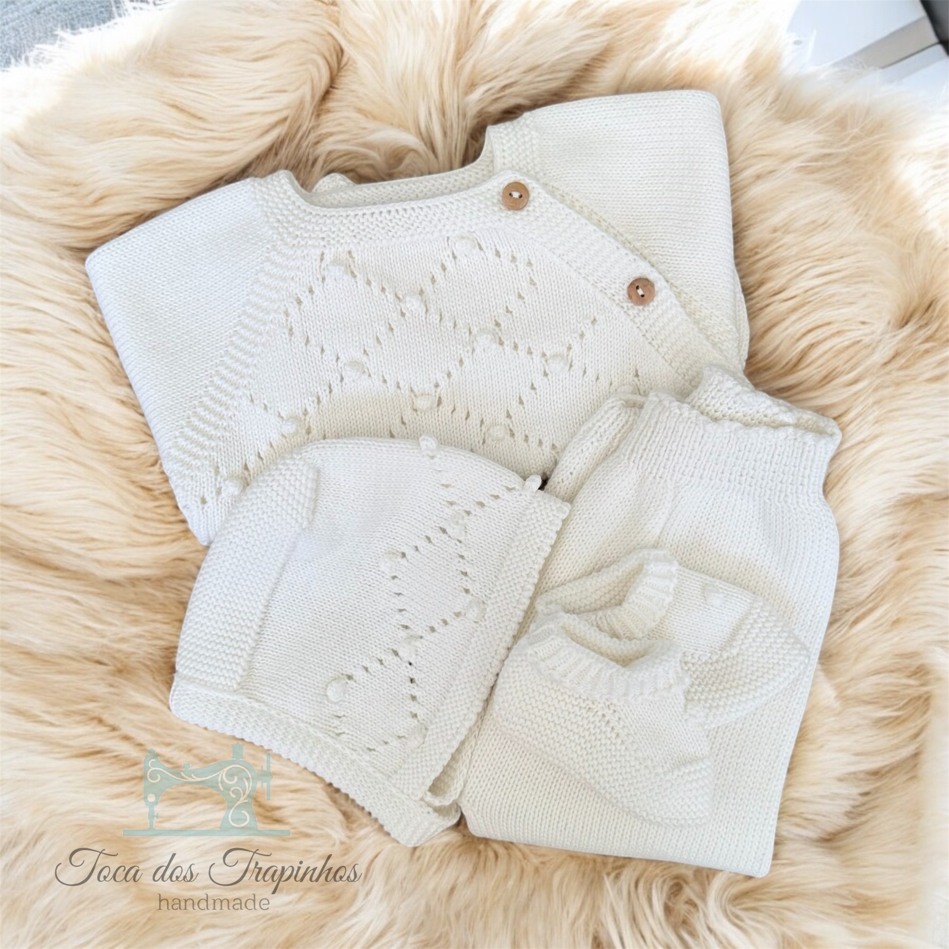 Conjunto de bebé malha creme com padrão corações e botões em fundo de pelo bege claro