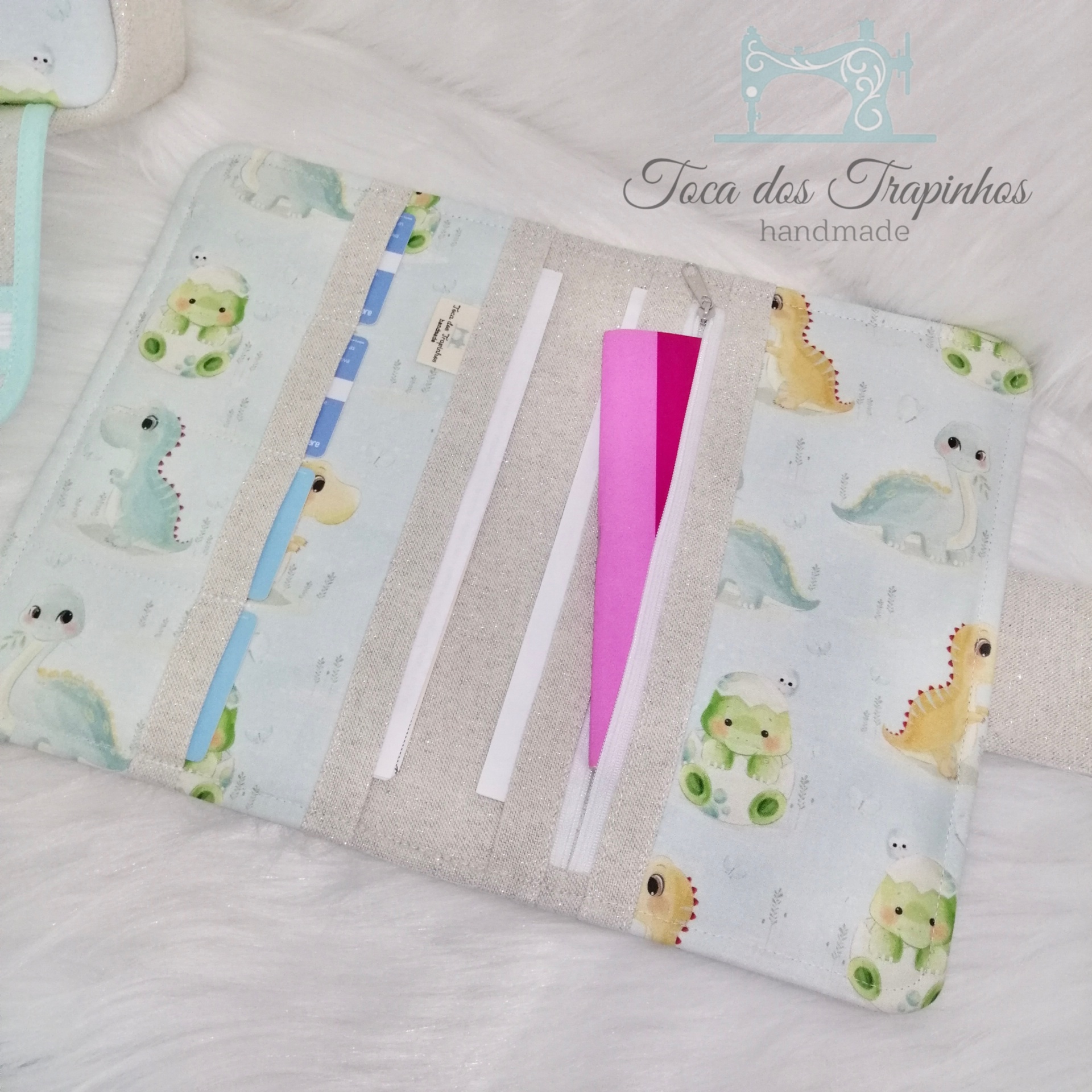 Estojo aberto de tecido com padrão de dinossauros coloridos em fundo azul claro