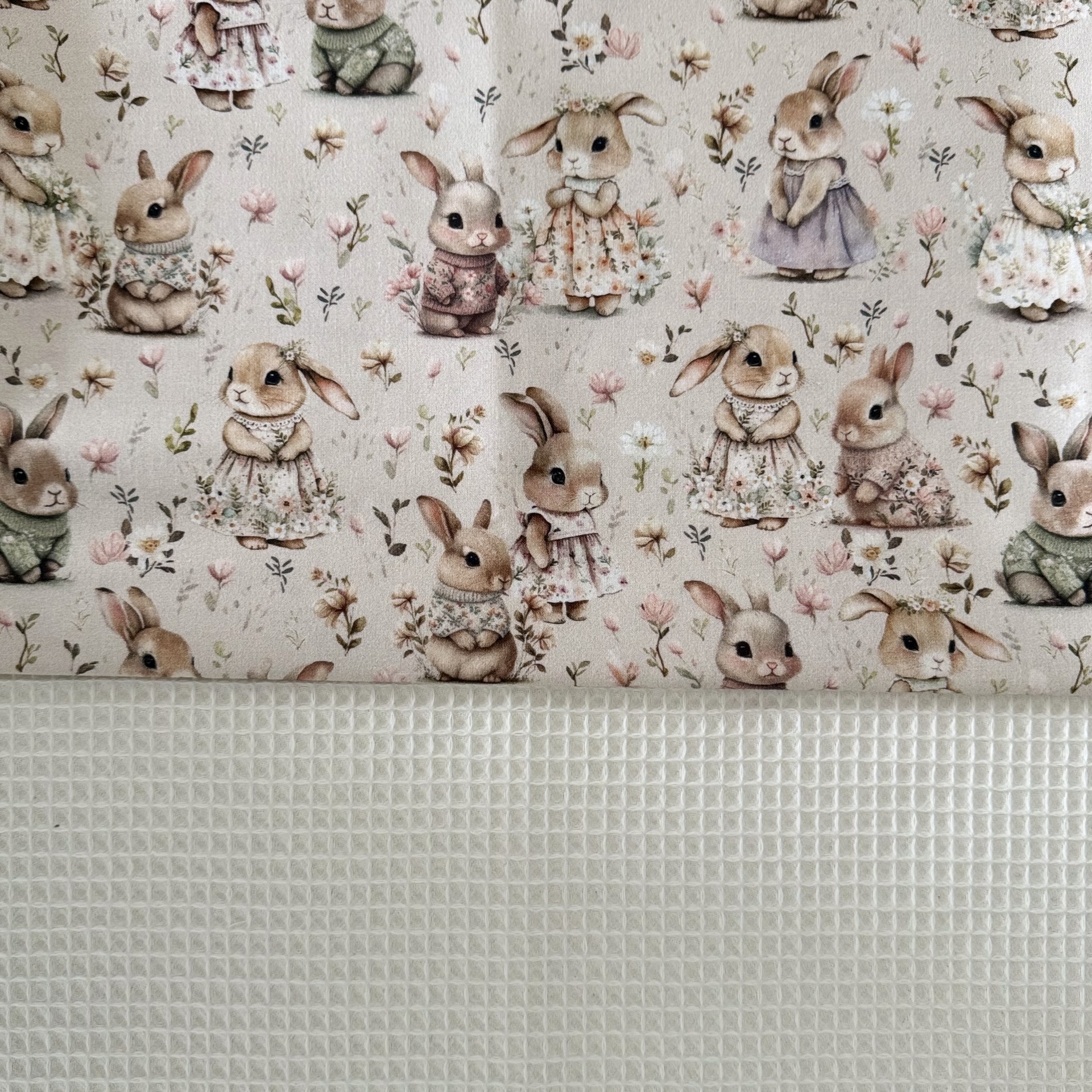 Tecido com padrão de coelhinhos em roupa colorida e tecido branco texturizado.