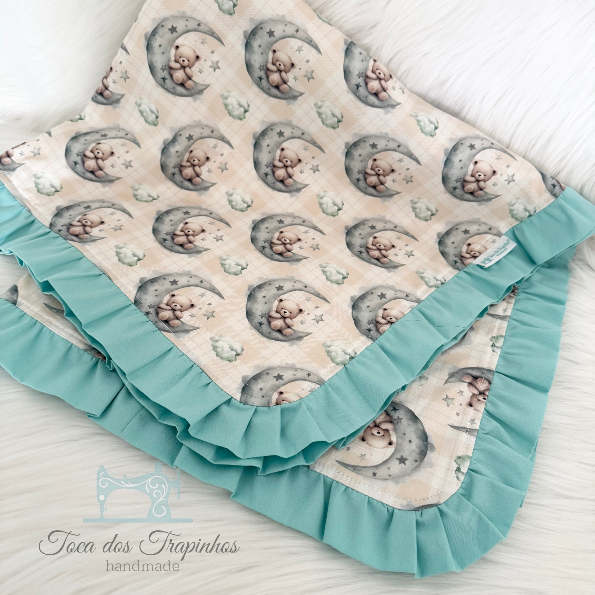 Manta de bebê com padrão de ursinhos, borda azul claro, sobre superfície branca felpuda