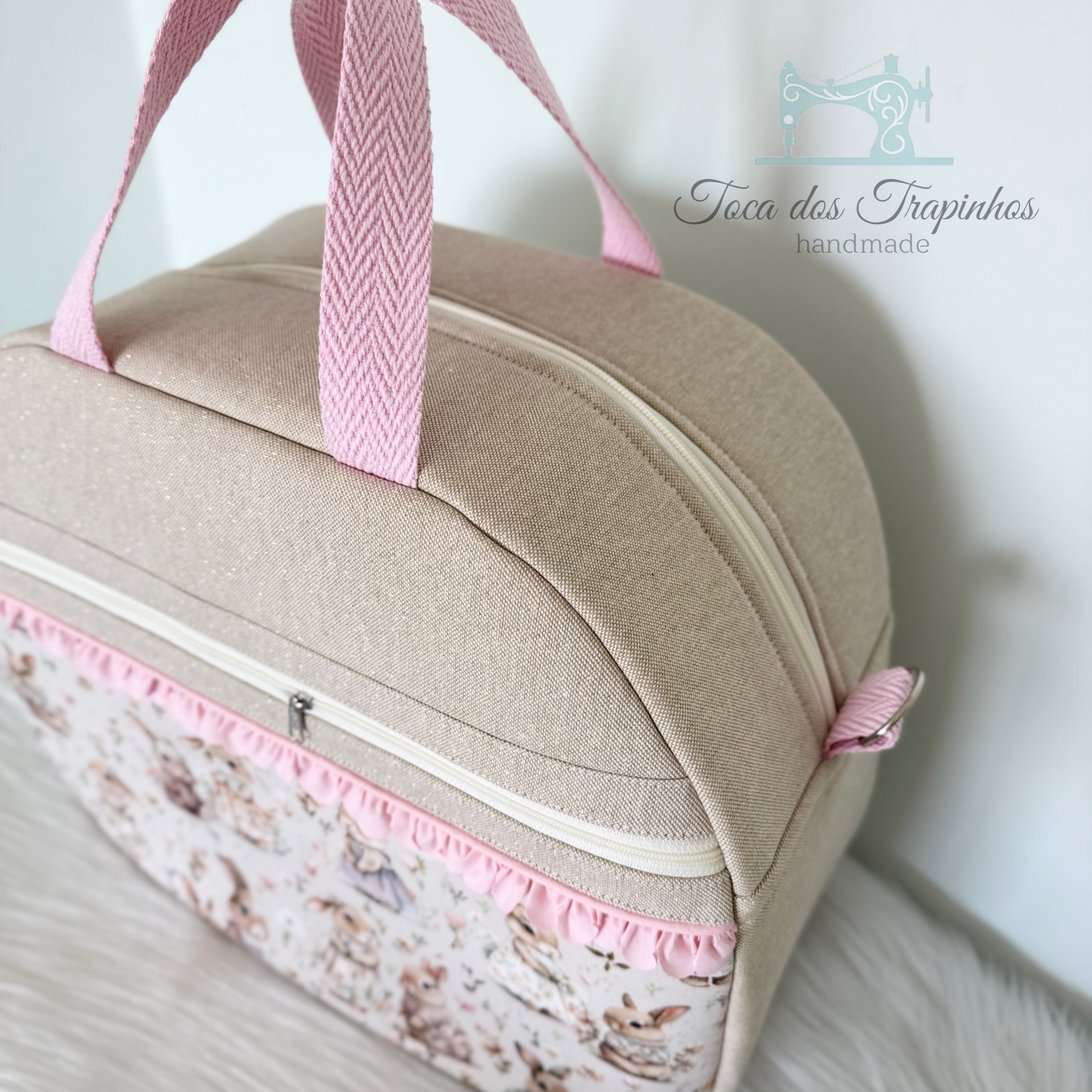Mala bege com pega rosa e padrão frontal com coelhos em tecido