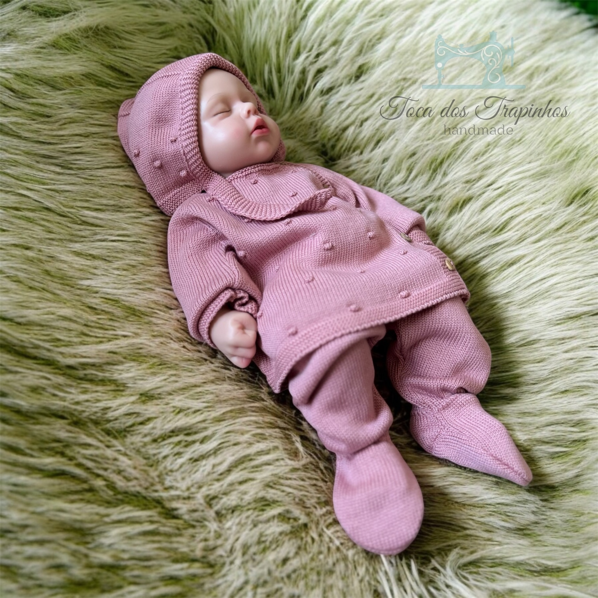 Boneca bebé com fato de malha rosa deitada em tecido verde felpudo