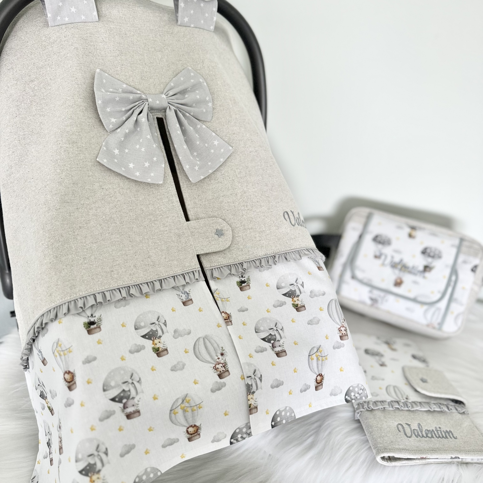 Capa para carrinho de bebé cinza clara com laço e estampa de balões e animais, com bolsa e porta-chupeta à vista