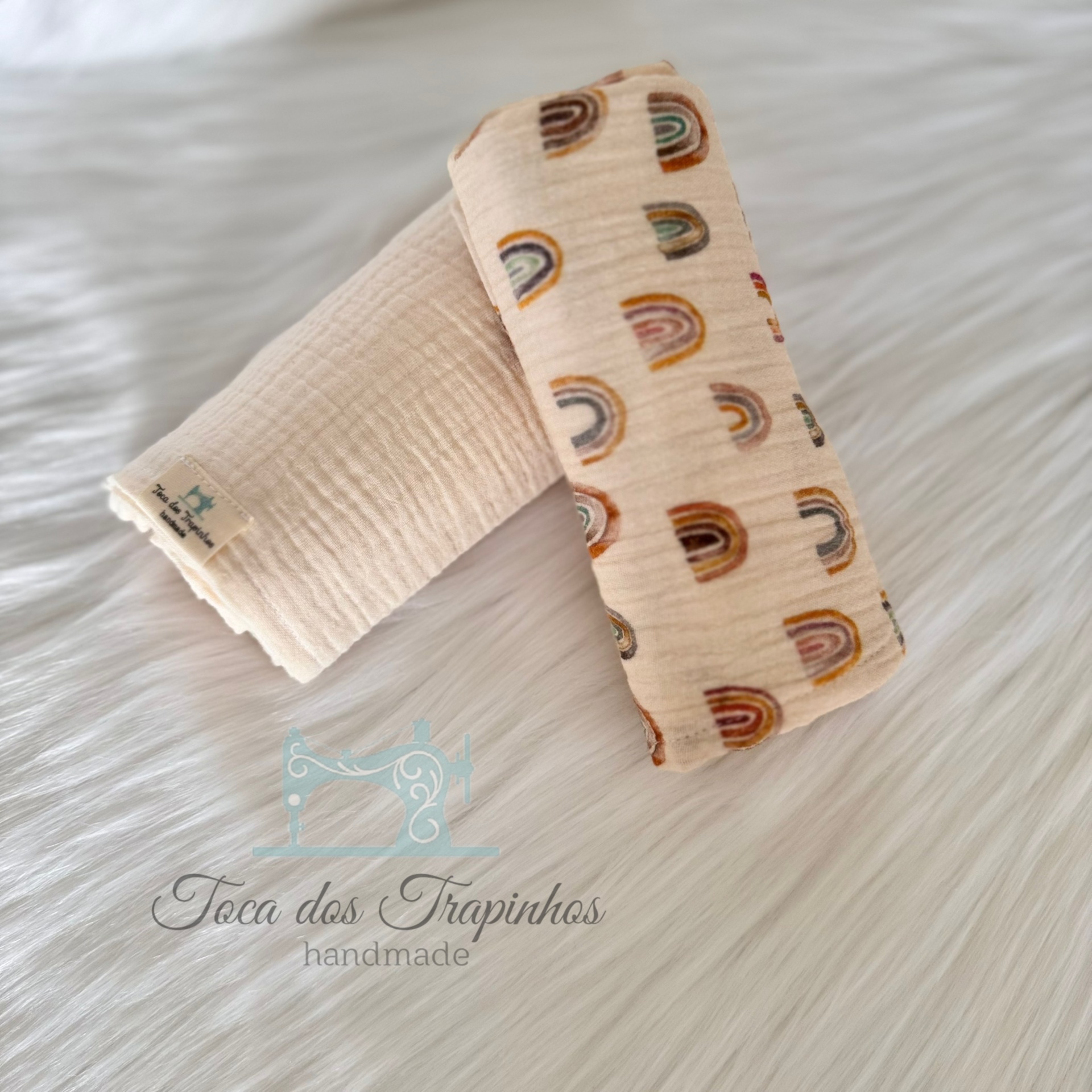 Dois panos de algodão cru, um liso e outro com padrão de arco-íris, sobre superfície branca macia