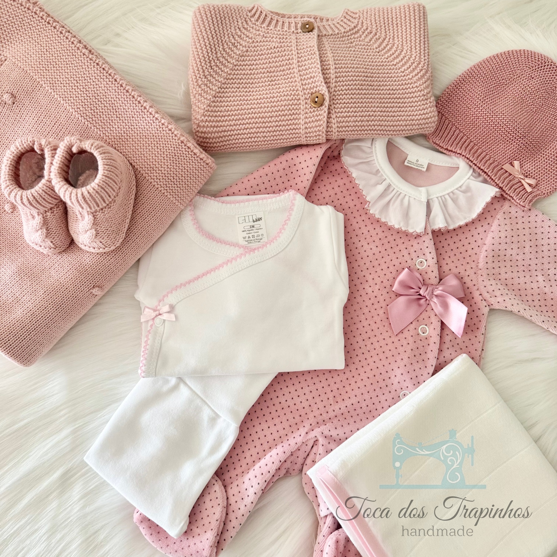 Conjunto de roupa de bebé rosa e branco com manta, sapatinhos, casaco e toalha bordada.