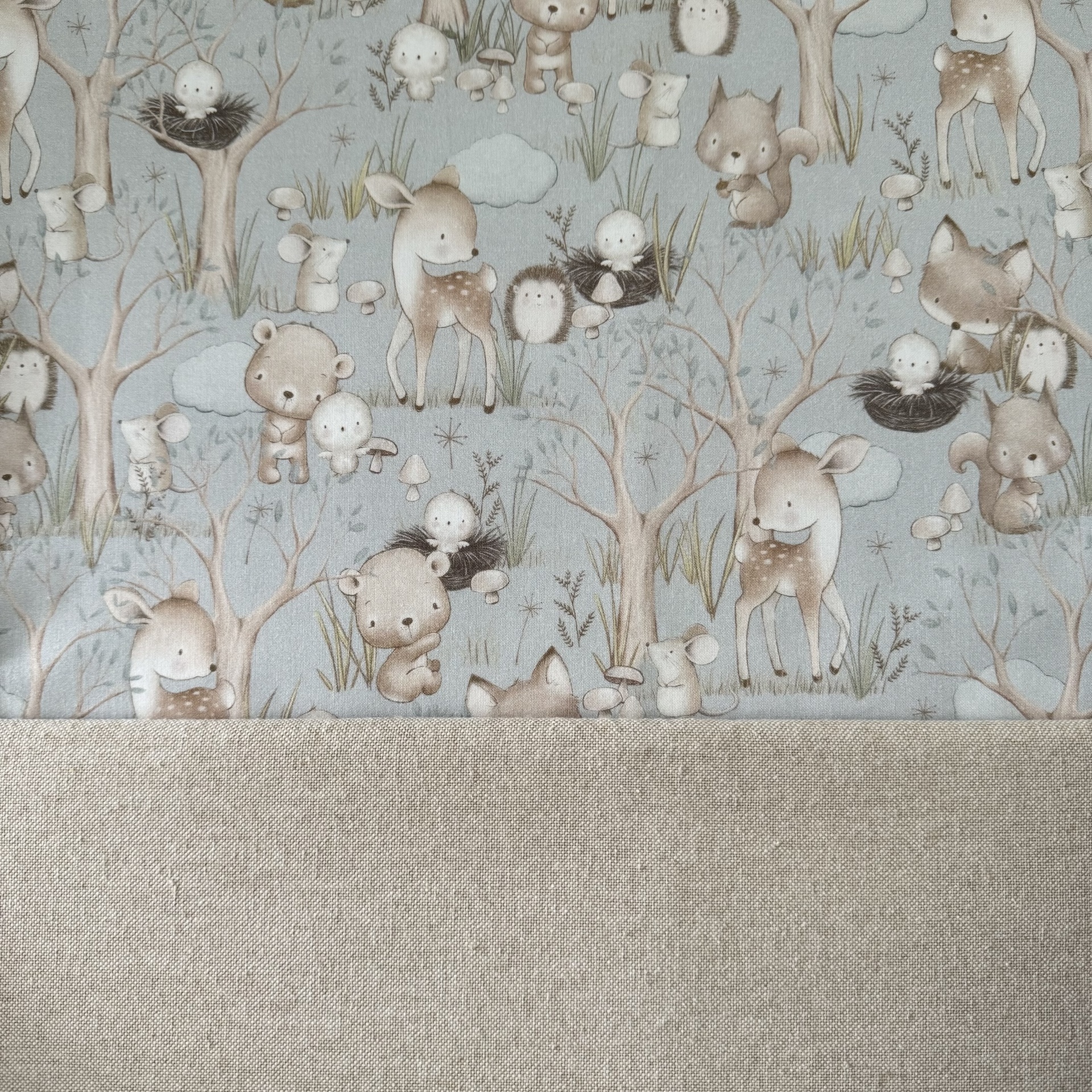 Tecido com padrão infantil de animais da floresta em tons pastel e tecido liso bege.