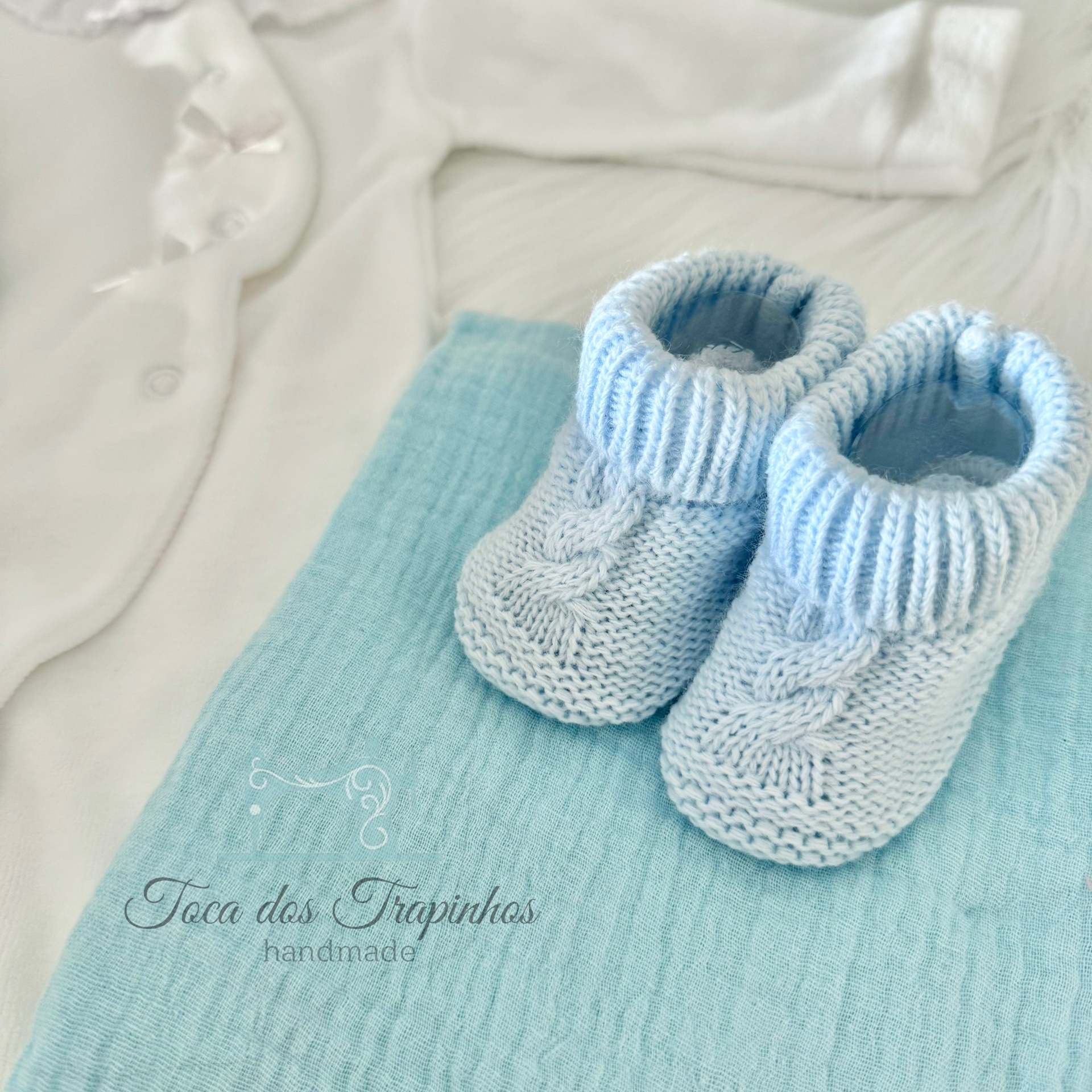 sapatinhos de bebé azuis em tricô com camisola branca e tecido azul turquesa